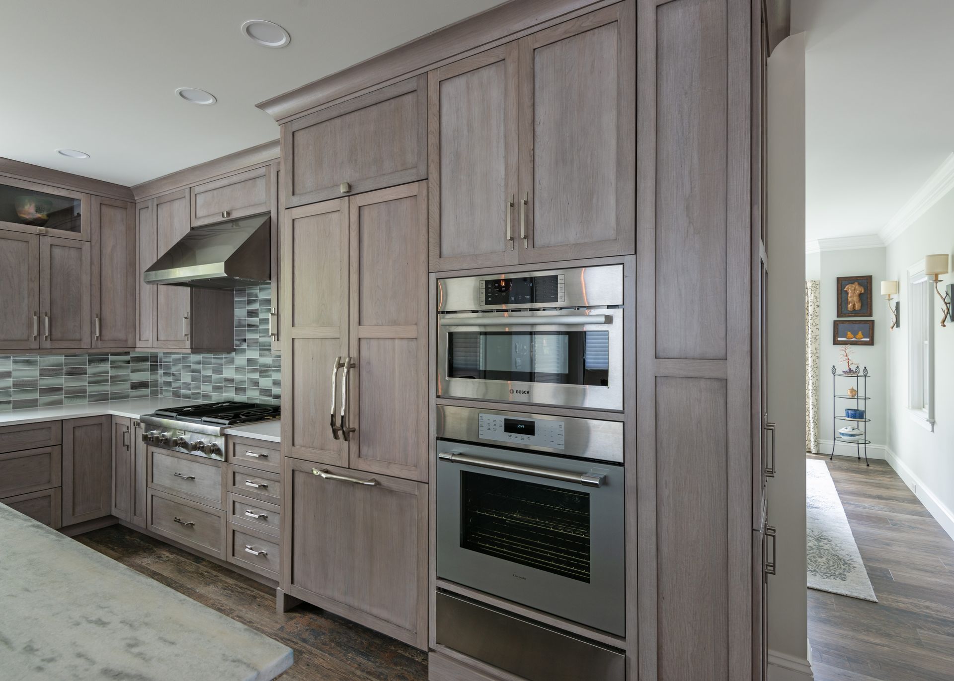 Modern kitchen with gray wood cabinets, built-in stainless steel appliances, and mosaic tile backsplash