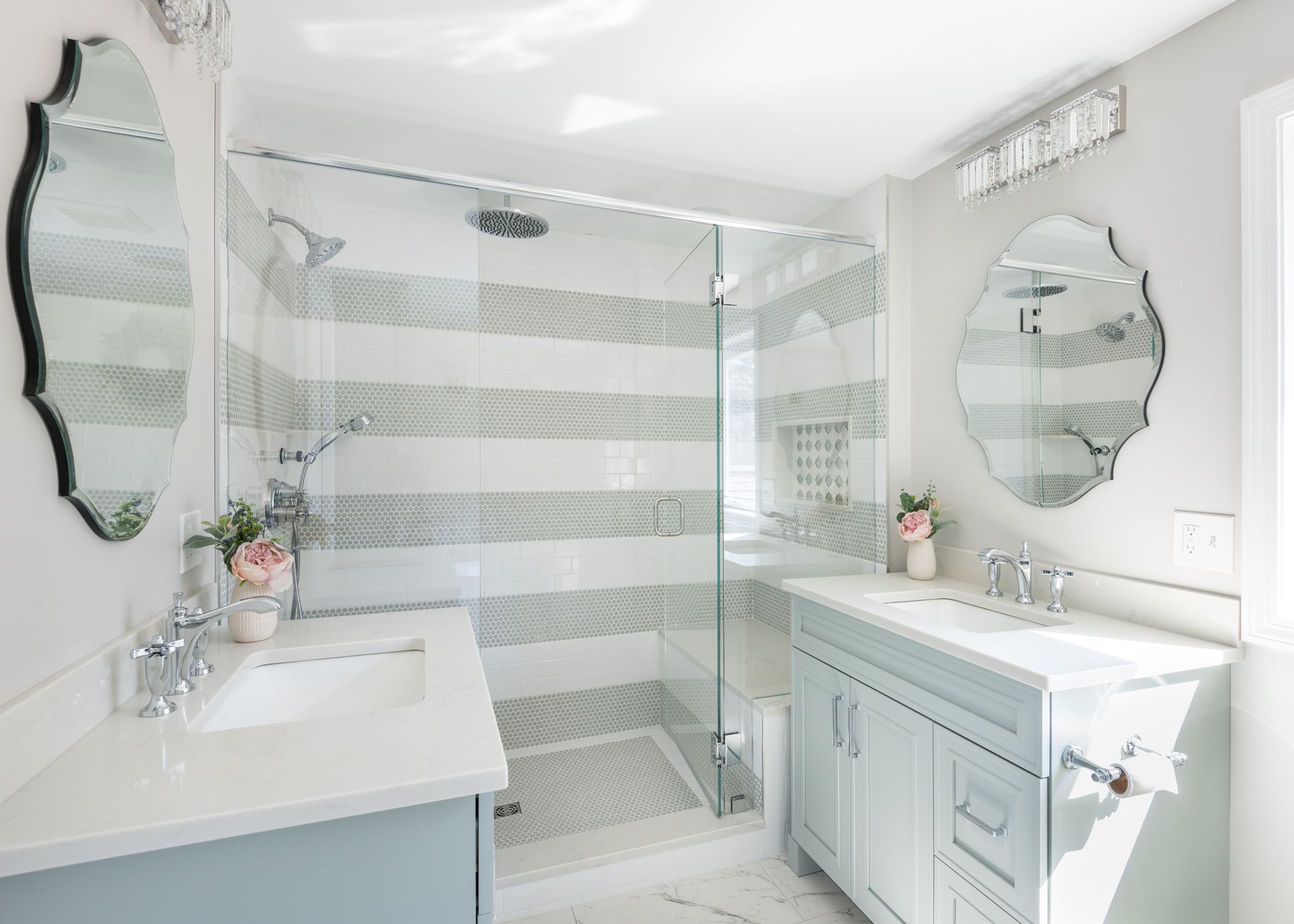 Bright white bathroom with double vanity, mirrored sinks, and glass shower with striped tile backsplash
