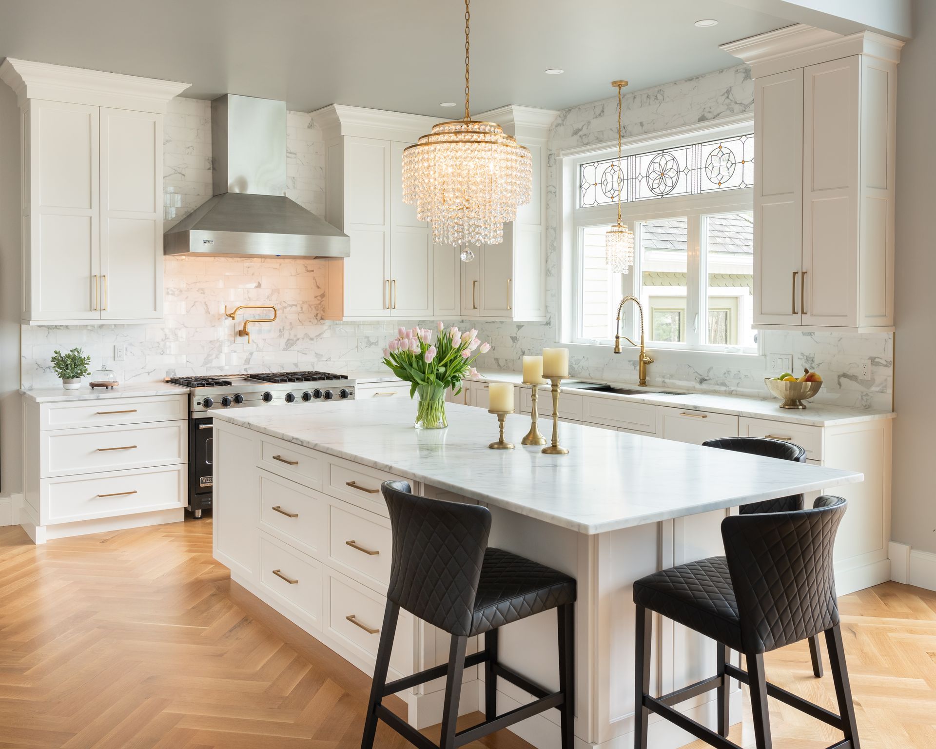 Bright modern kitchen with white cabinets, marble island, black stools, and a crystal pendant light