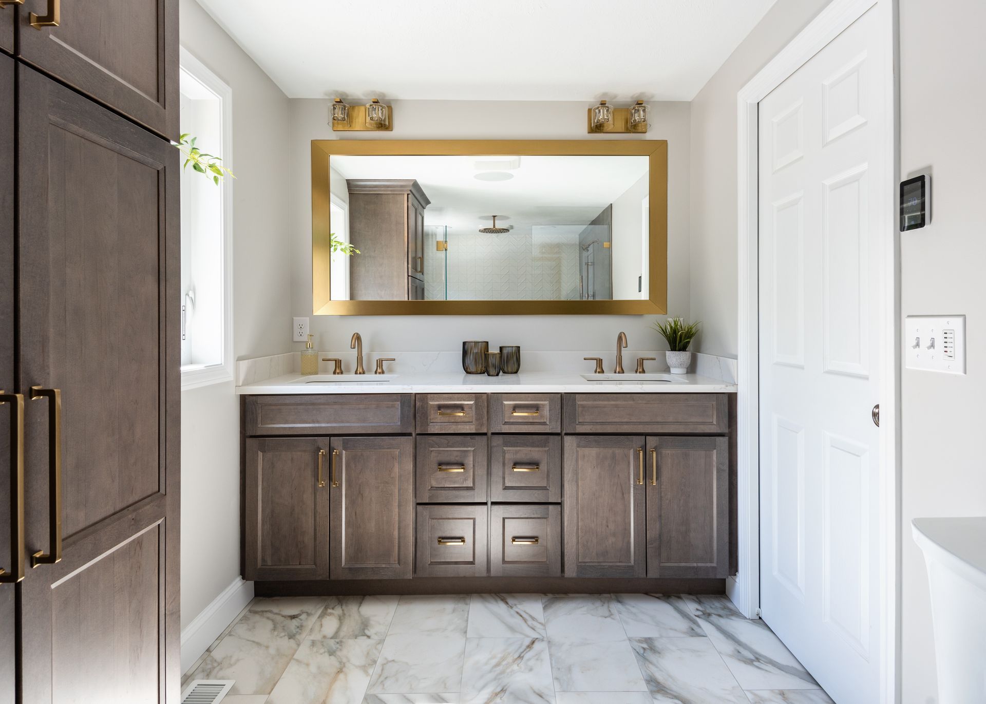 Modern bathroom with dark wood double vanity, large gold-framed mirror, and marble tile floor.