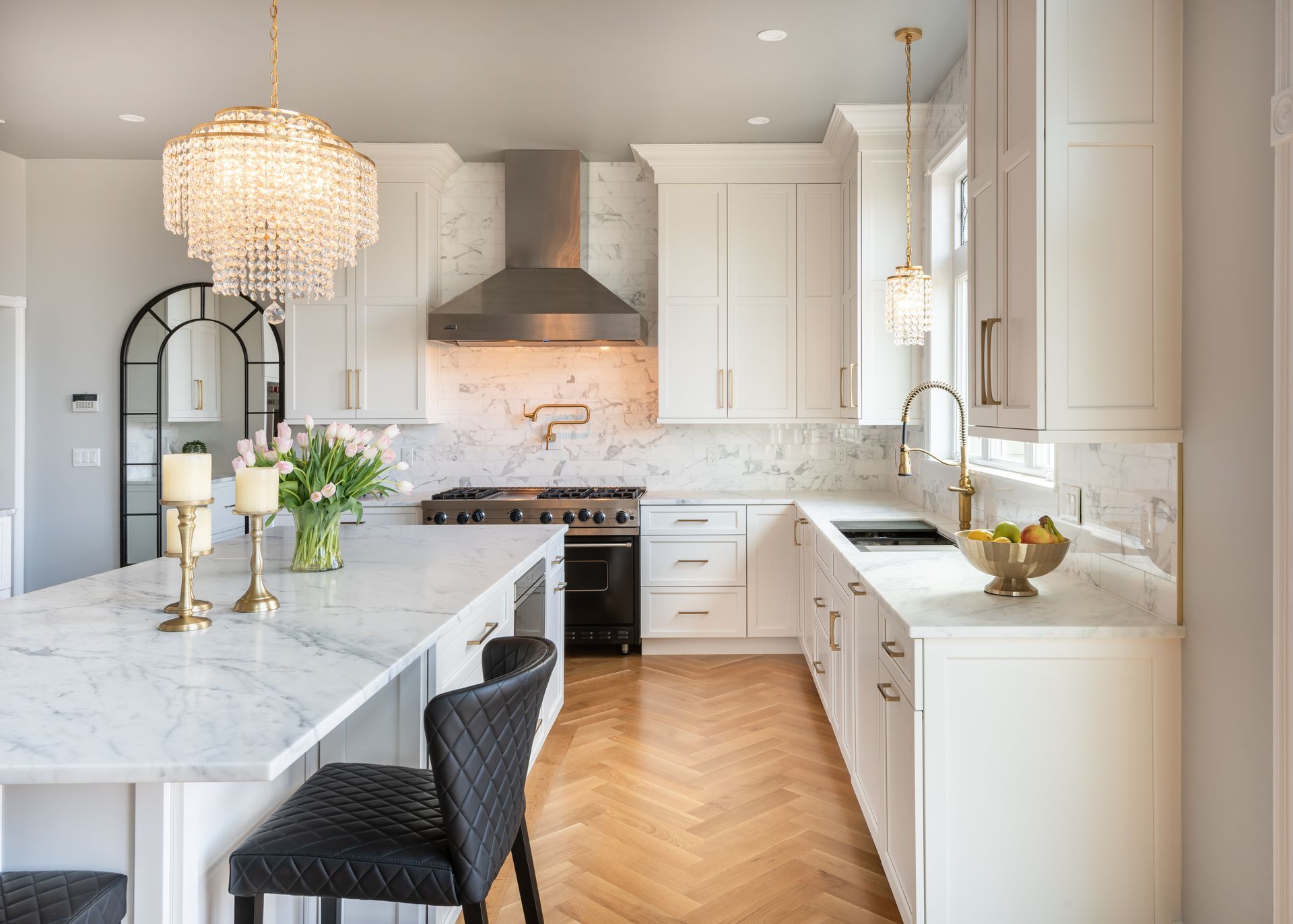 Bright modern white kitchen with marble counters, black stools, and stainless steel range hood