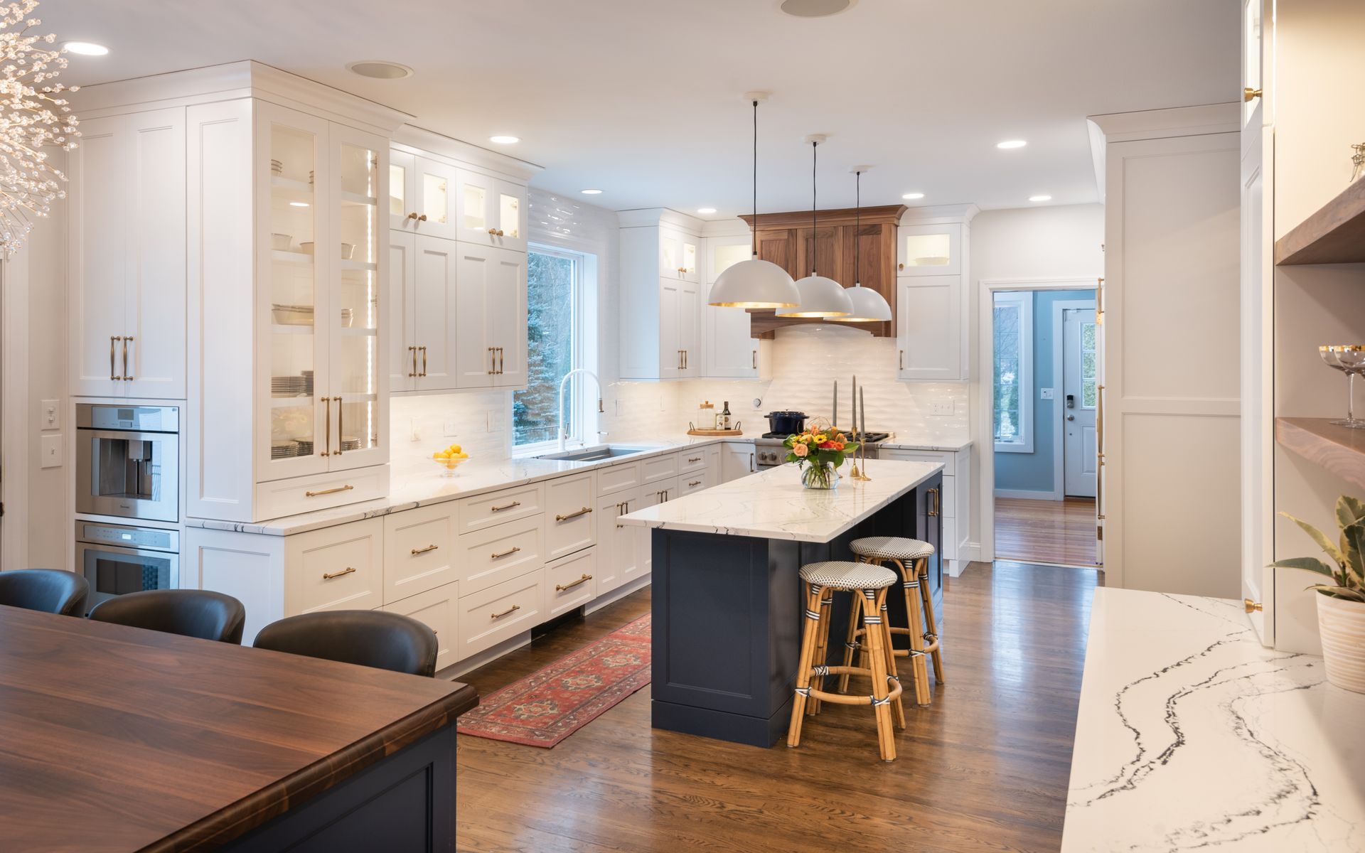 Bright, modern kitchen with white cabinets, marble island, wood floors, and stools under pendant lights.