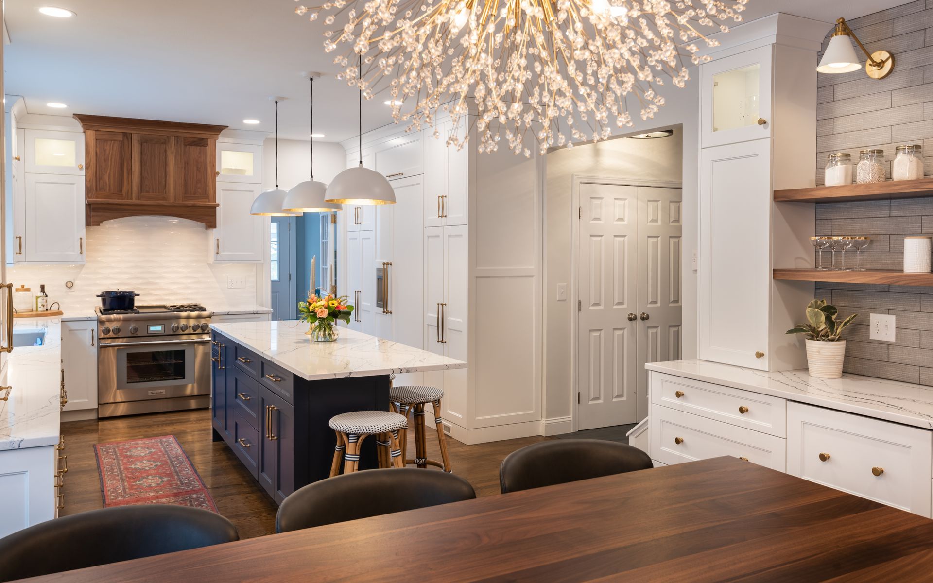 Bright modern kitchen with dark island, white cabinets, pendant lights, and chandelier over a dining table