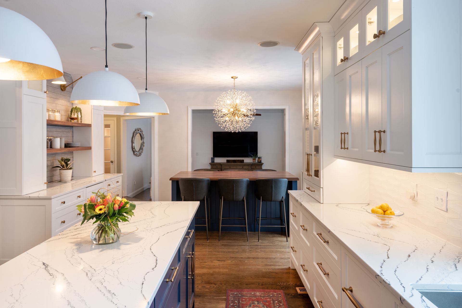Bright modern kitchen with white marble islands, pendant lights, blue stools, and a dining table in the background