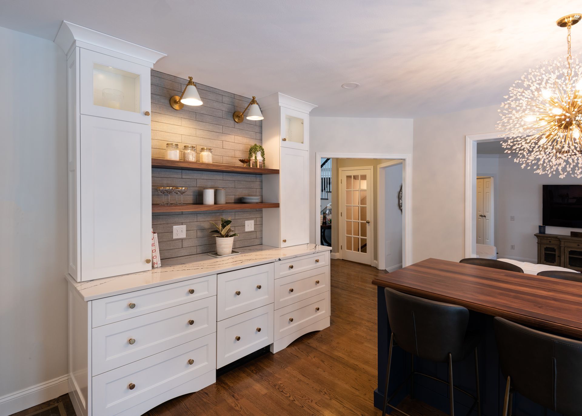 Bright dining room with white cabinetry, wood table, pendant lights, and a mirrored tile backsplash.