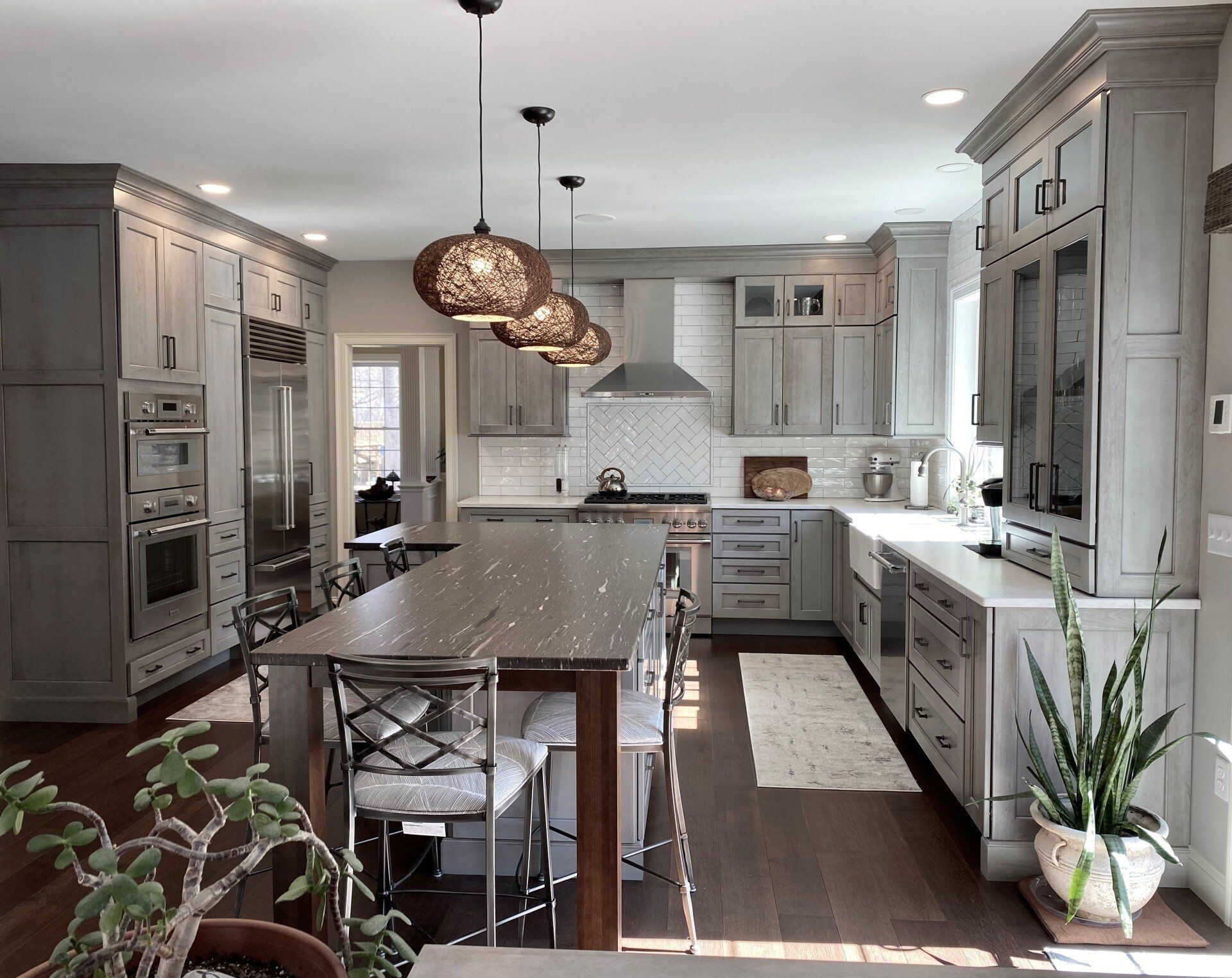 Bright modern kitchen with gray cabinets, island seating, pendant lights, and dark wood floors
