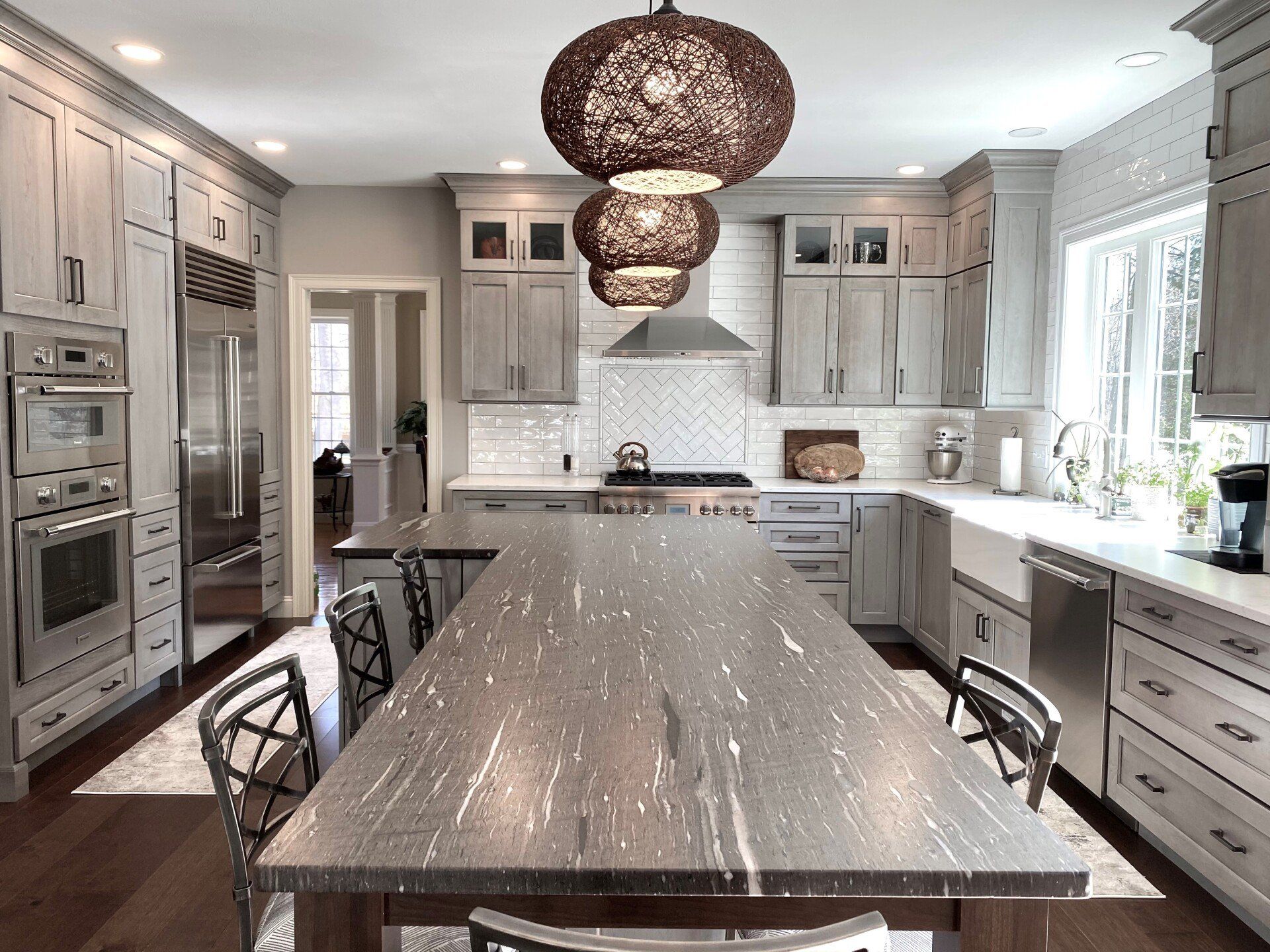 Bright modern kitchen with gray cabinets, marble island, pendant lights, and large windows