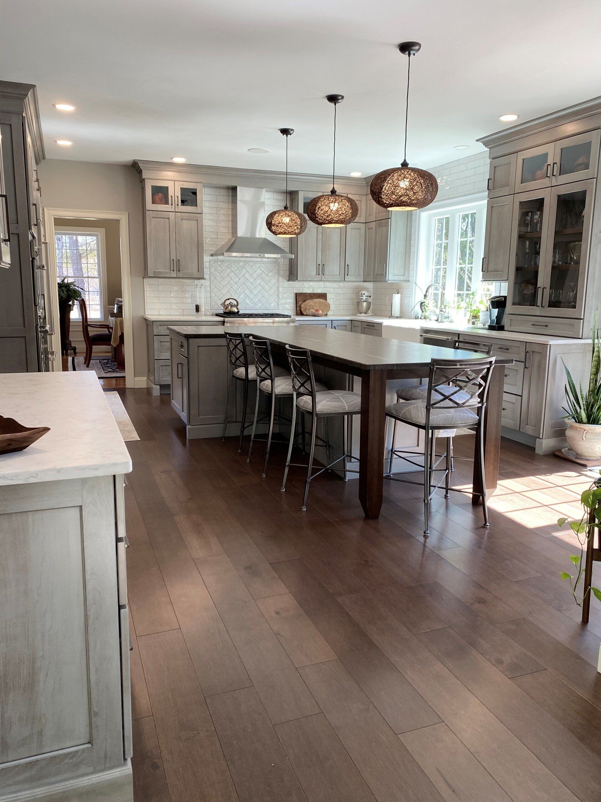Bright white kitchen with large island, pendant lights, bar stools, and dark wood floors