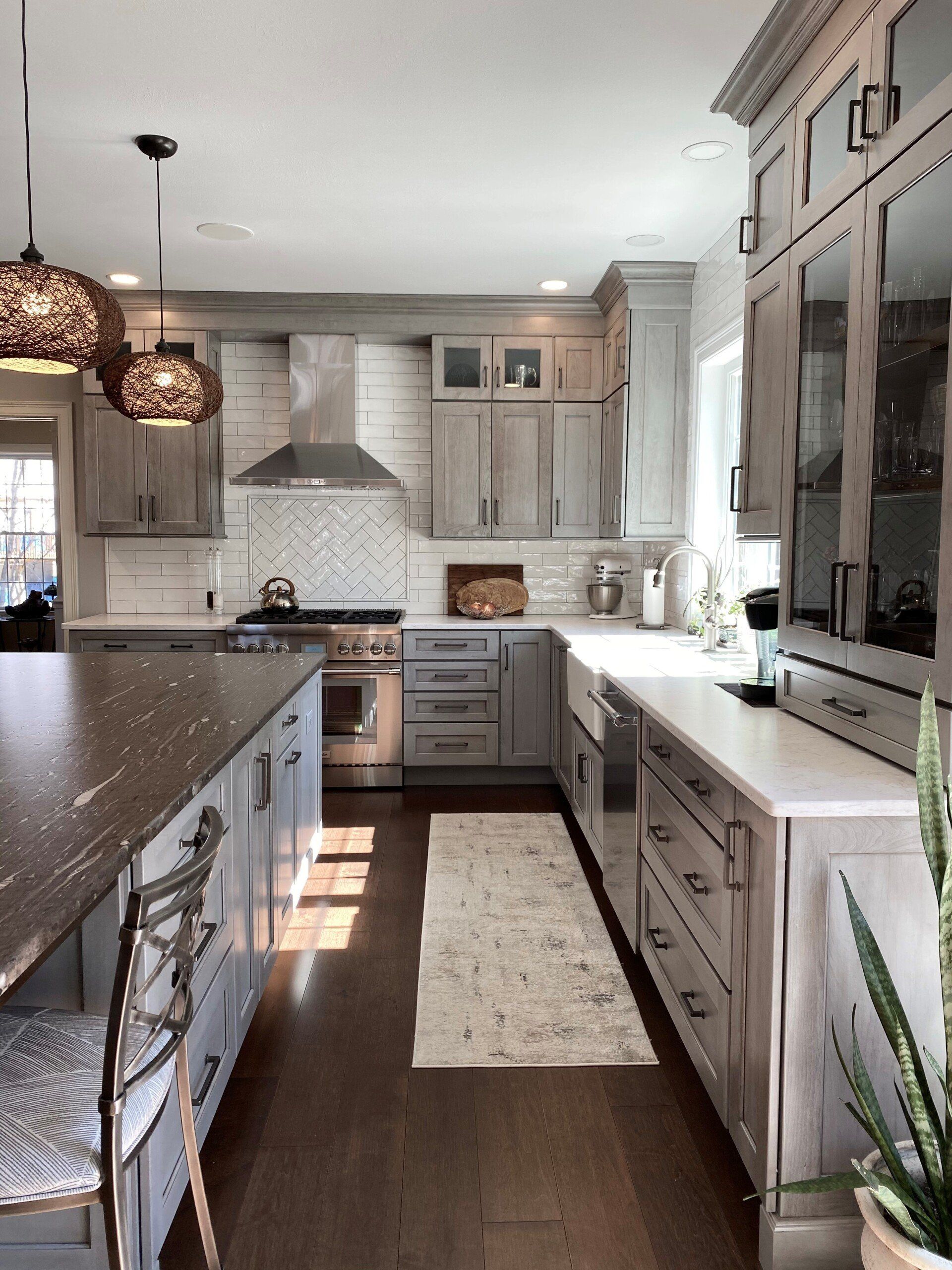 Bright kitchen with white cabinets, dark island, pendant lights, and a long runner rug.