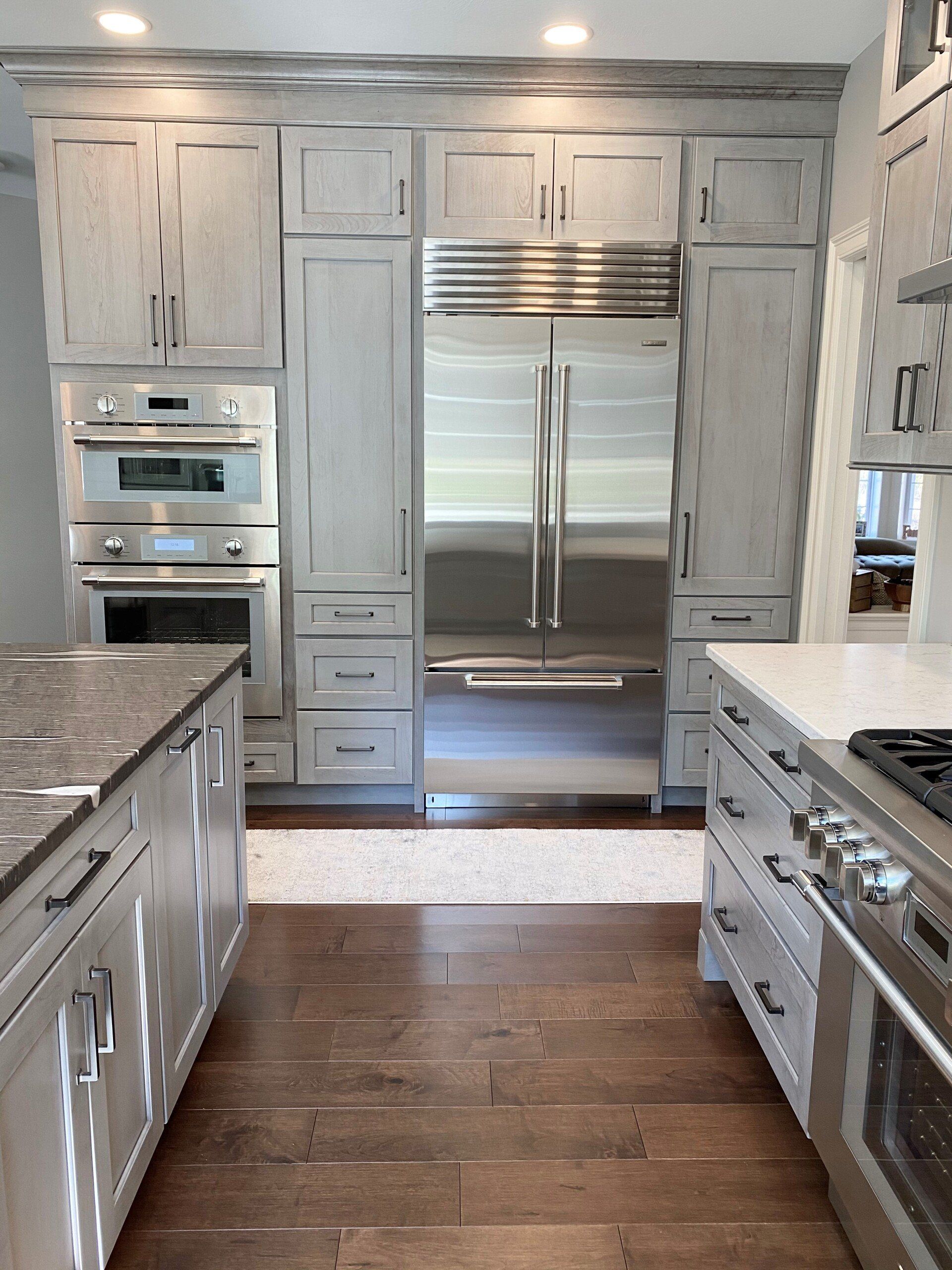Modern kitchen with stainless steel double refrigerator, white cabinets, granite counters, and hardwood floor