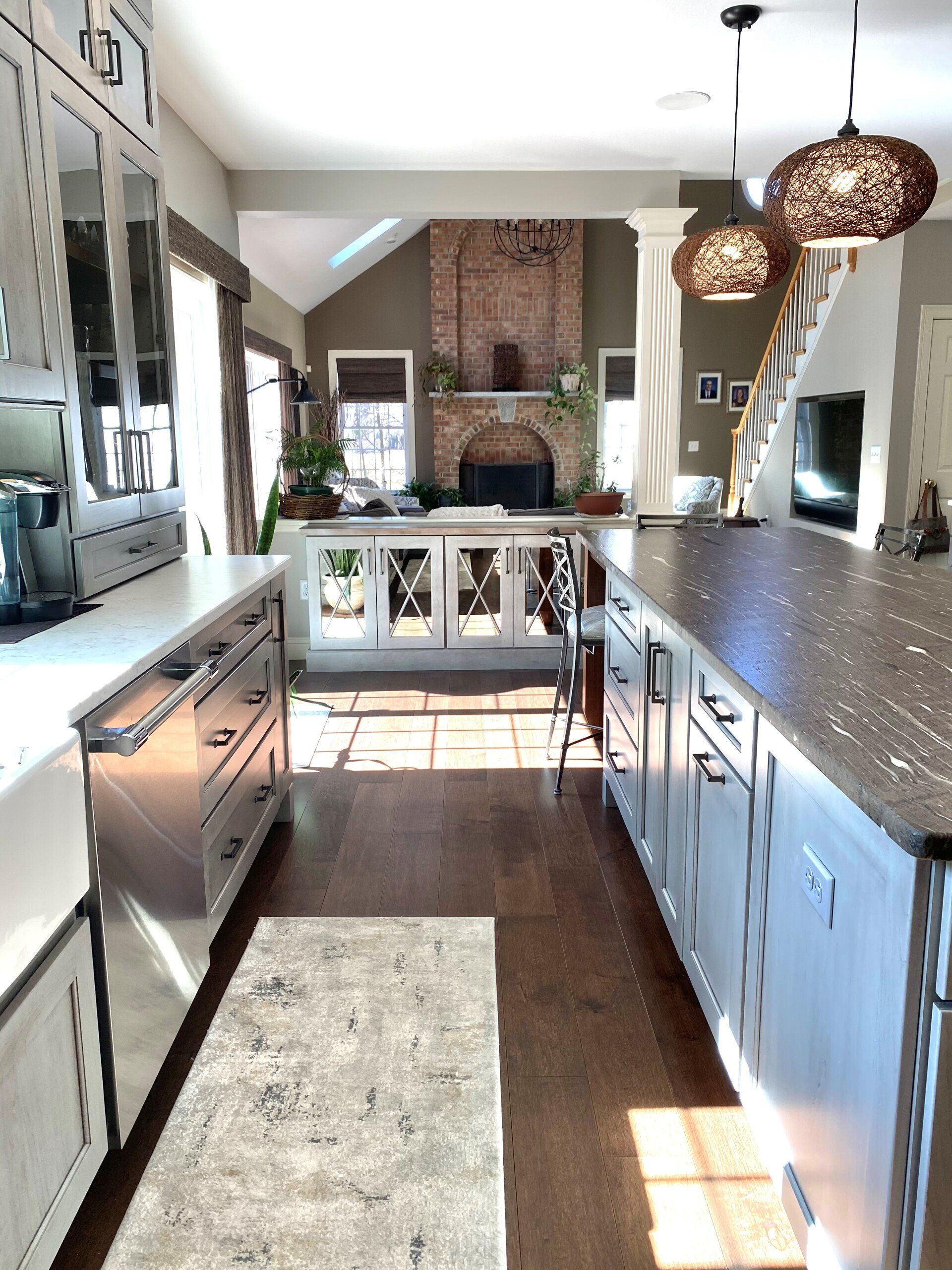 Bright kitchen with stainless appliances, blue-gray cabinets, pendant lights, and a brick fireplace in back.