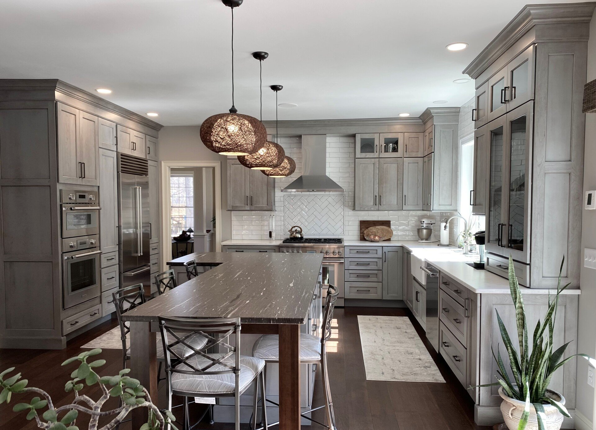 Bright modern kitchen with gray cabinets, a large island, pendant lights, and a potted plant in the corner