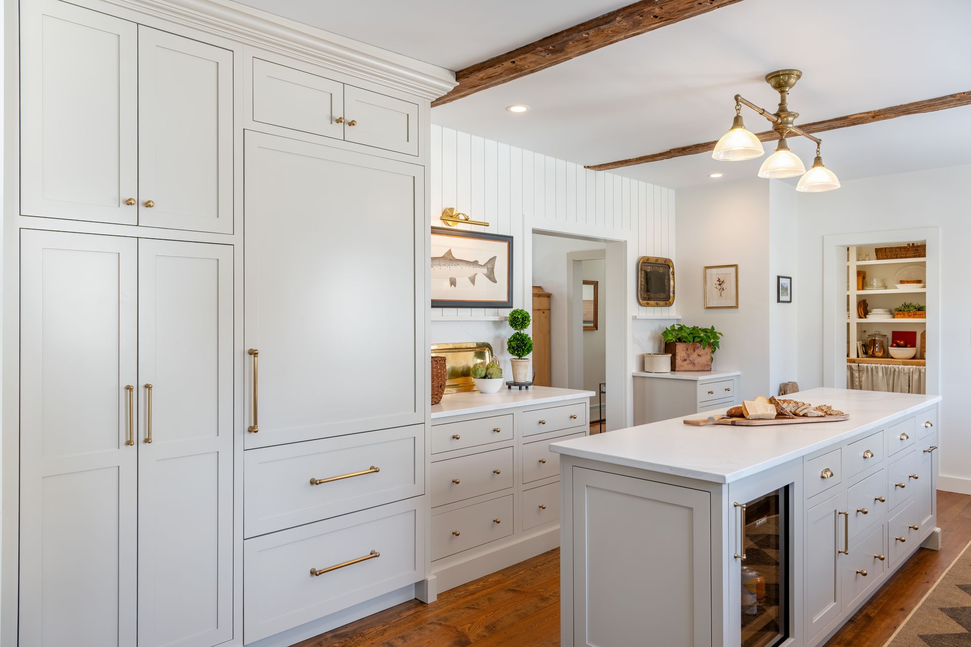 Bright white farmhouse kitchen with built-in cabinets, island, and warm wood ceiling beams