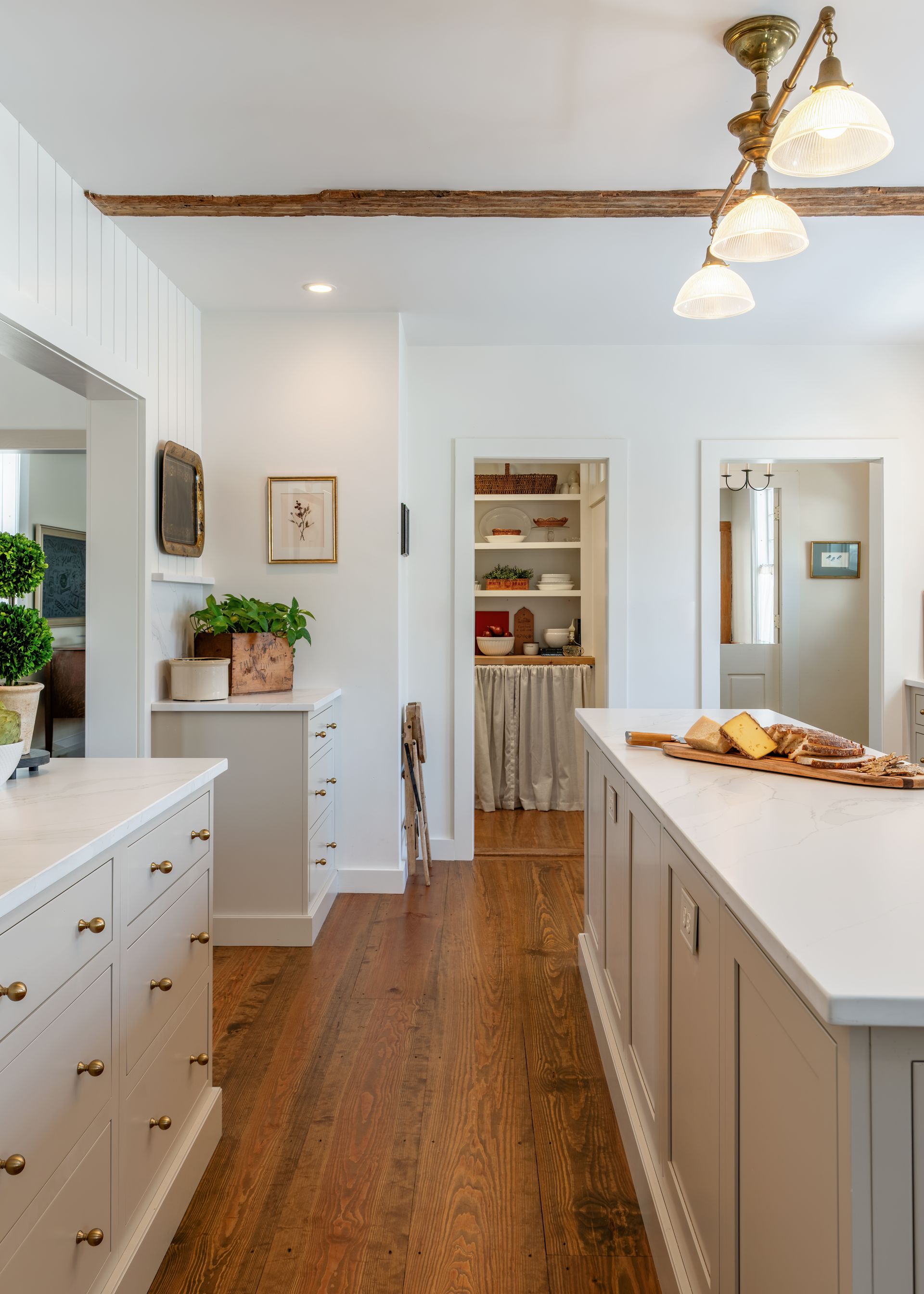 Bright farmhouse kitchen with white cabinets, wooden floors, and a central island under pendant lights.
