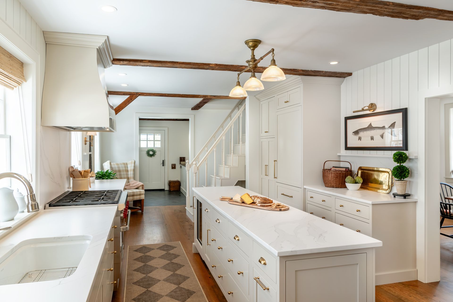 Bright farmhouse kitchen with white cabinets, central island, wood beams, and a hanging light fixture