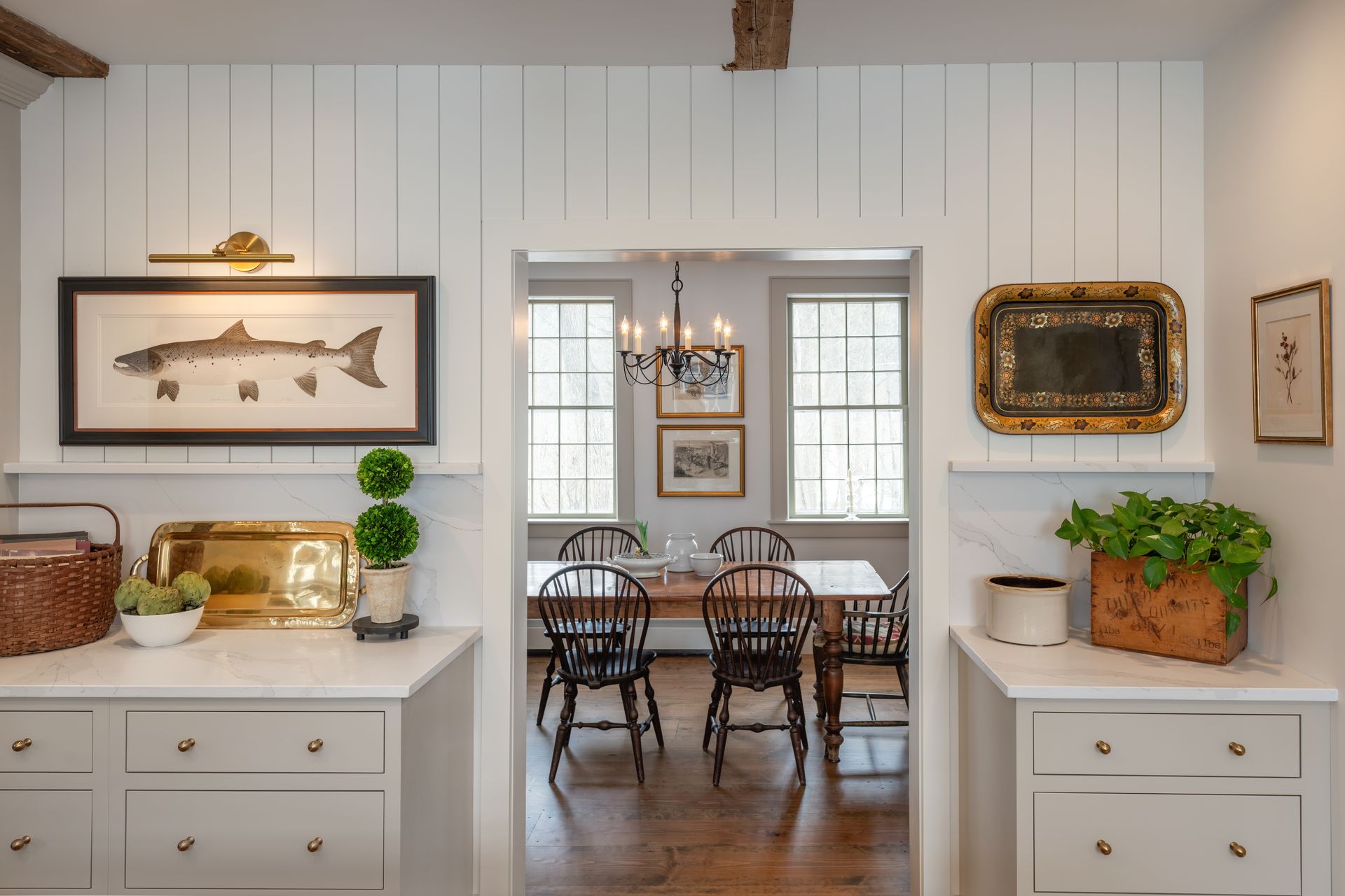 Bright farmhouse dining room with white-paneled walls, dark wood table, and vintage decor