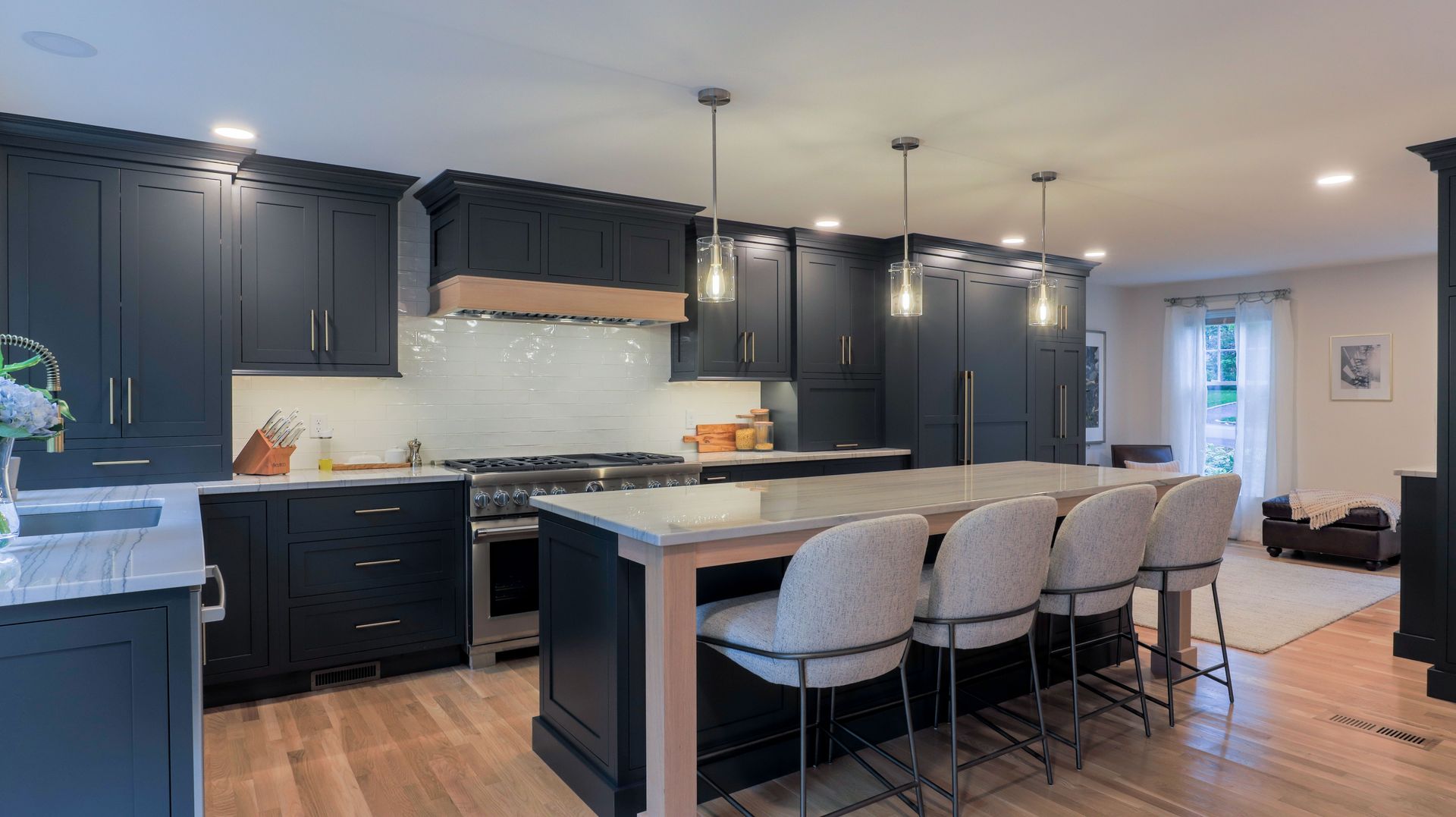 Modern kitchen with dark cabinets, large island, pendant lights, and beige barstools