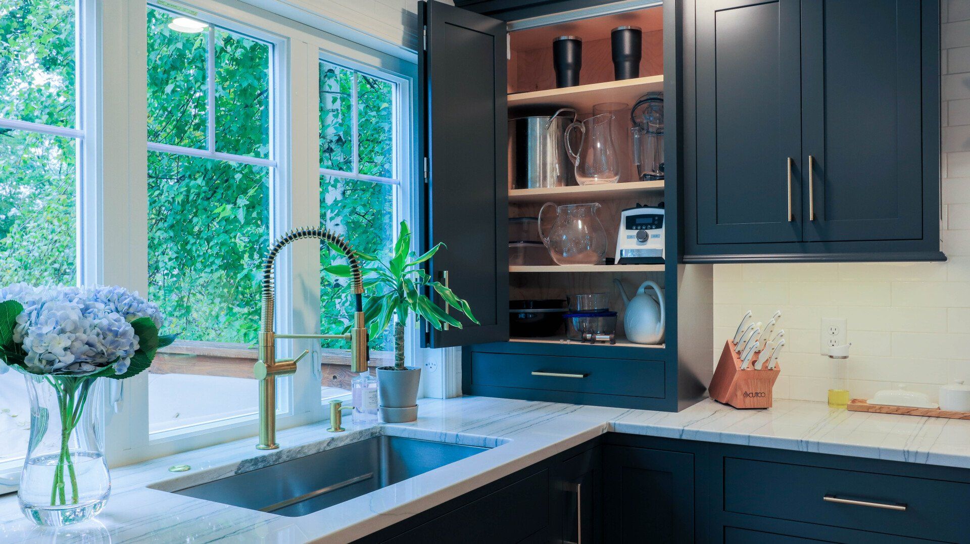 Modern kitchen sink by a bright window, with dark cabinets, open shelving, and a vase of flowers.