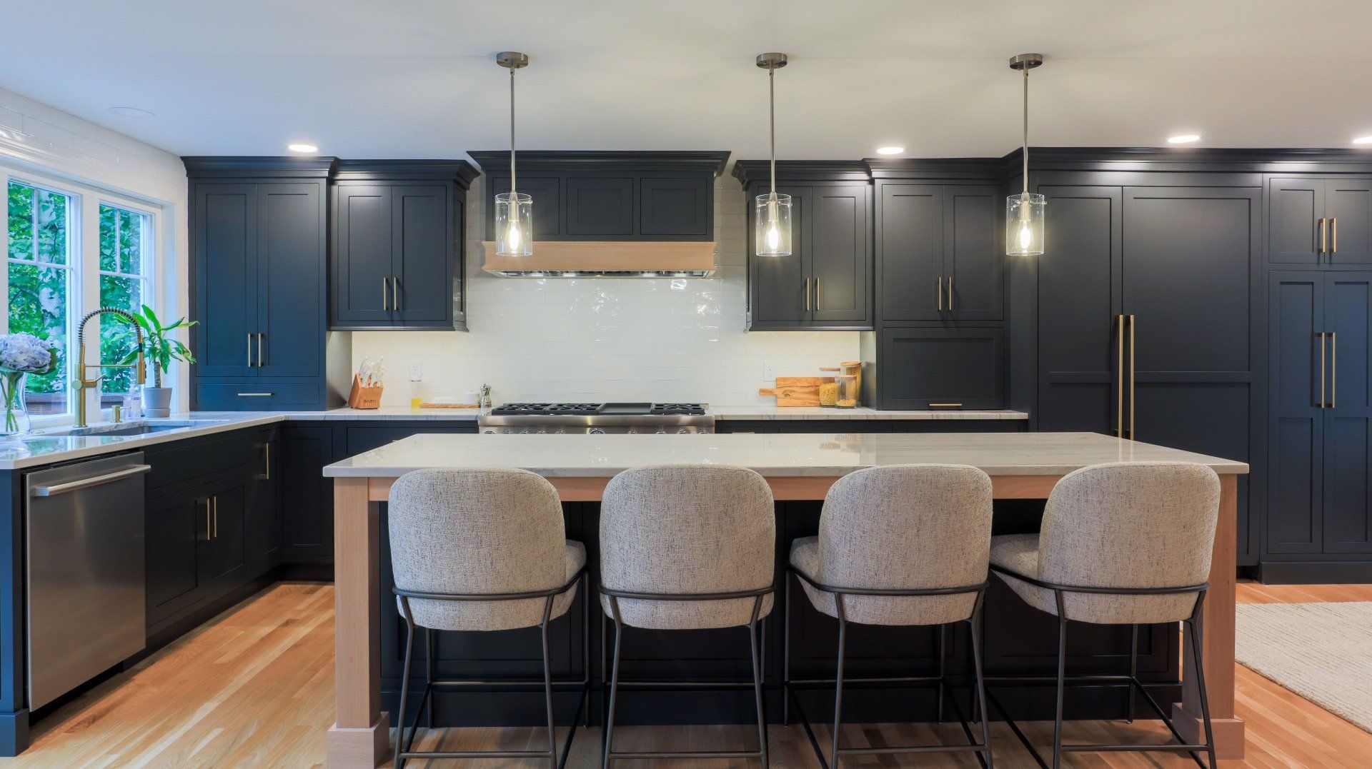 Modern kitchen with dark cabinets, large island, pendant lights, and four upholstered stools