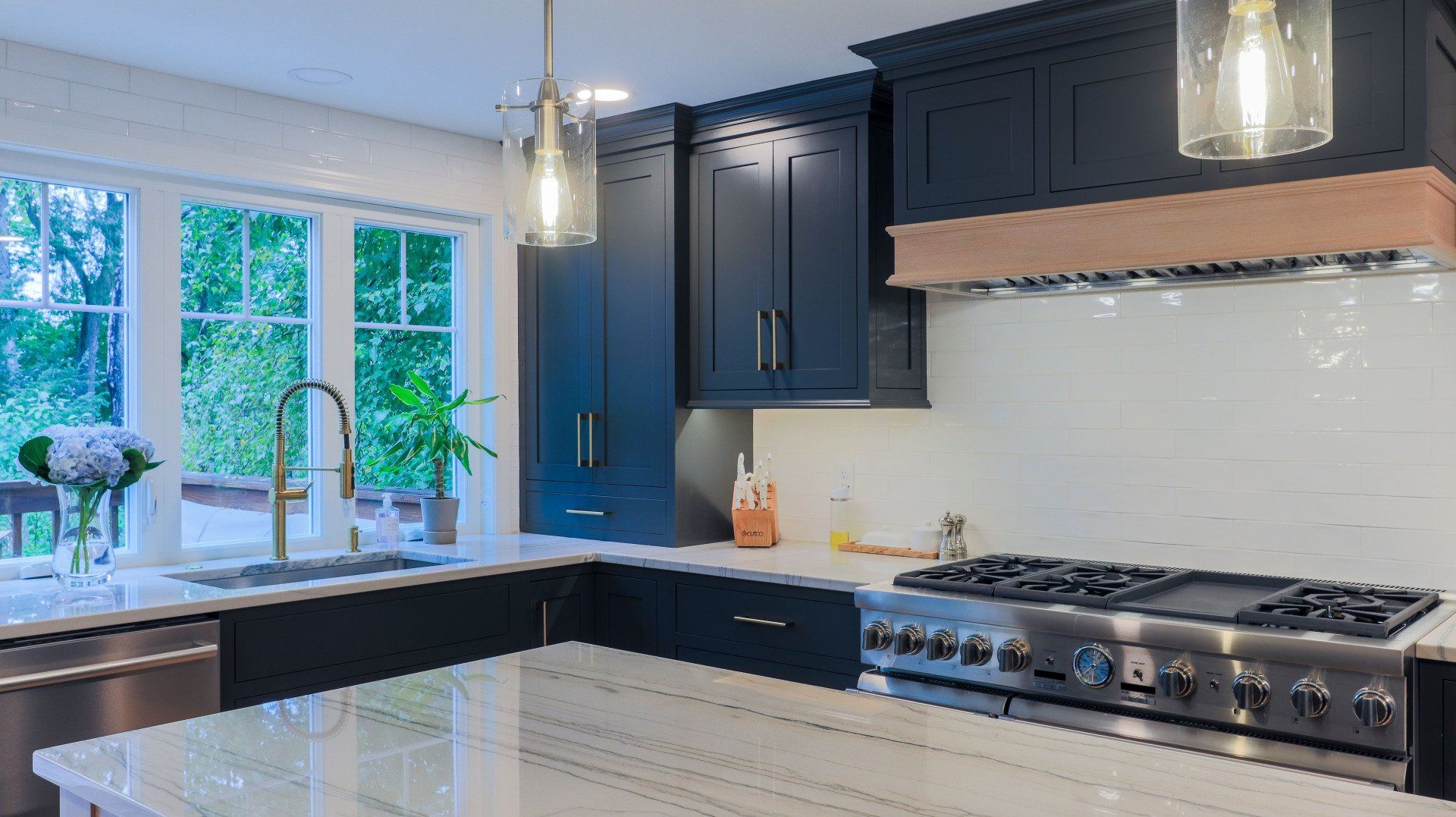 Modern kitchen with navy cabinets, white countertops, gas range, and large window over the sink