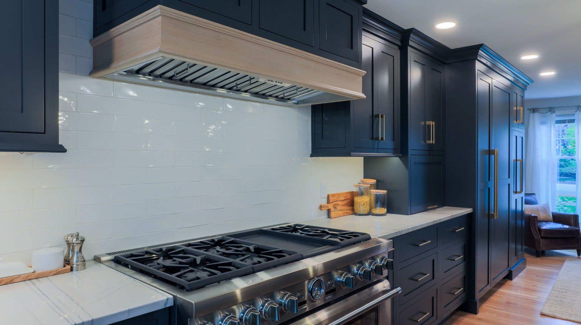 Modern kitchen with navy cabinets, gas range, white backsplash, and bright windowed dining area.