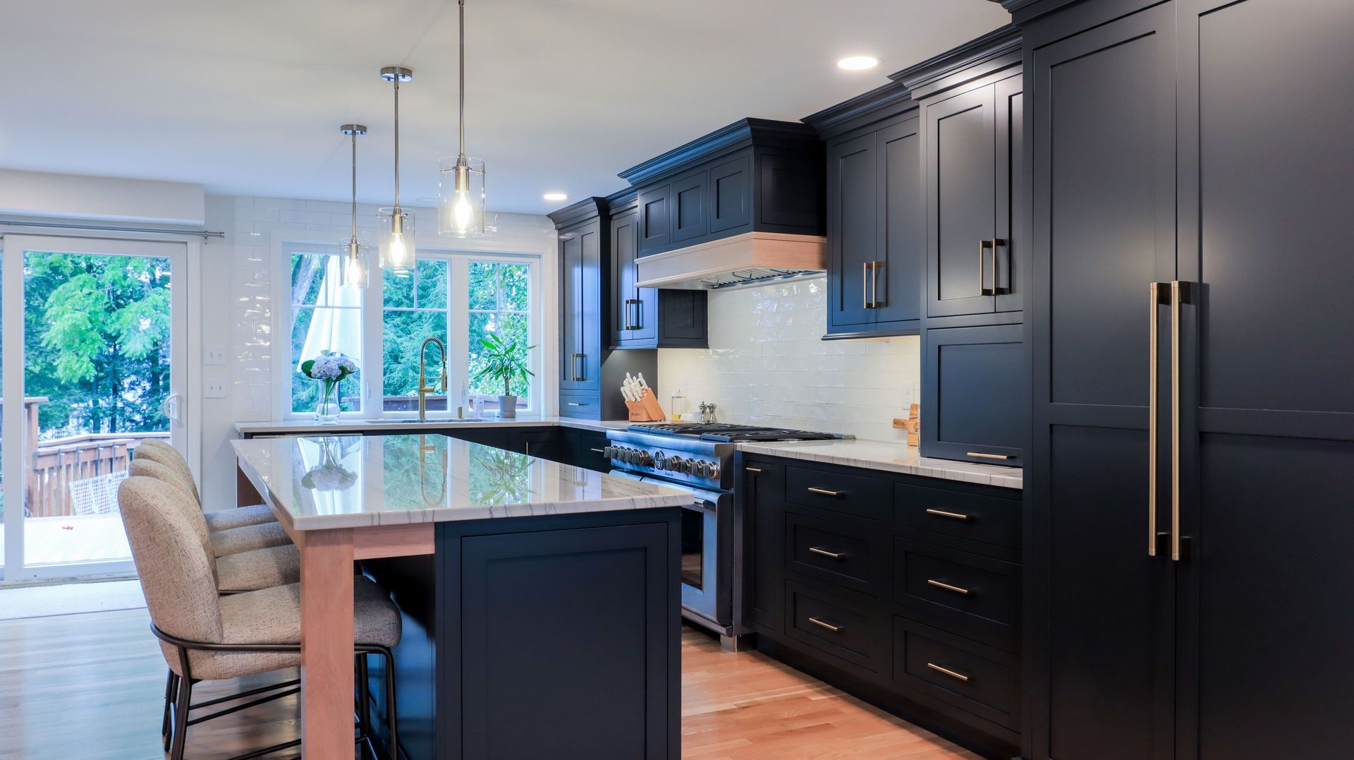 Modern kitchen with dark cabinets, large island, bar stools, pendant lights, and bright windows