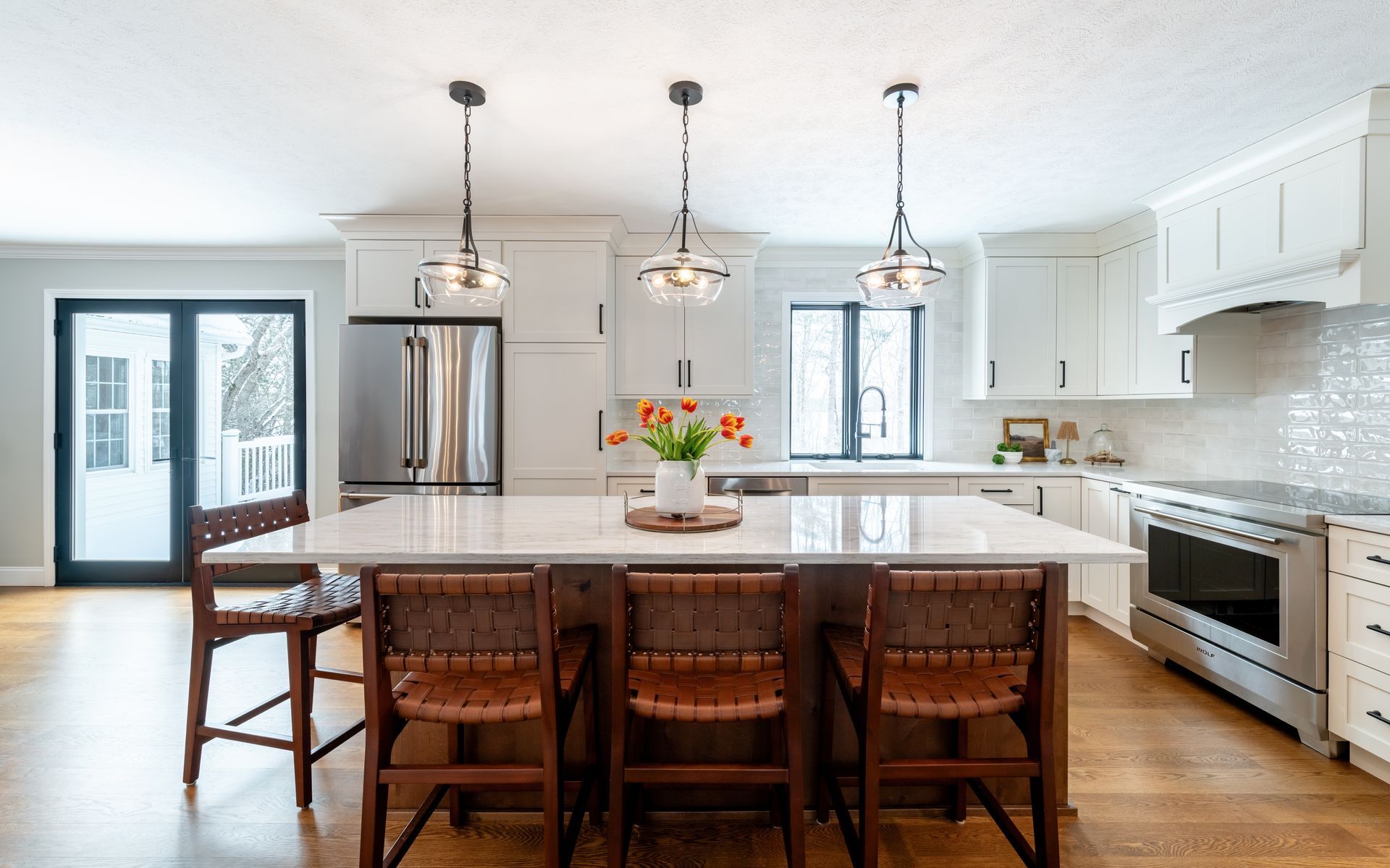 Bright modern kitchen with island, wooden stools, white cabinets, stainless appliances, and pendant lights