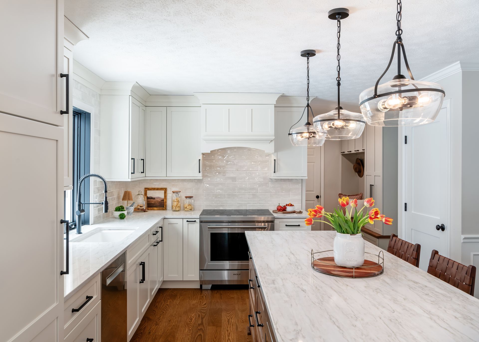 Bright white kitchen with island, pendant lights, stainless stove, and flowers on a wooden table
