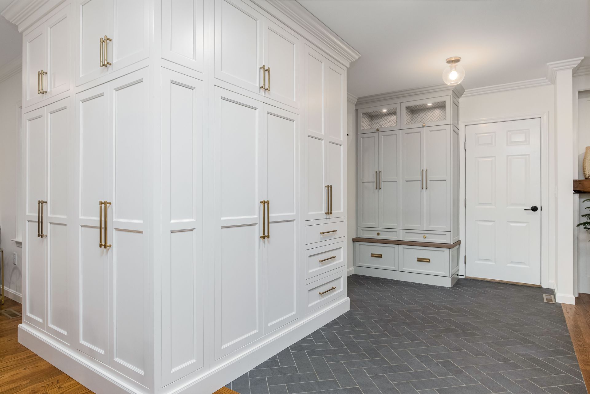 White built-in mudroom cabinets with brass hooks and a bench in a bright entryway.