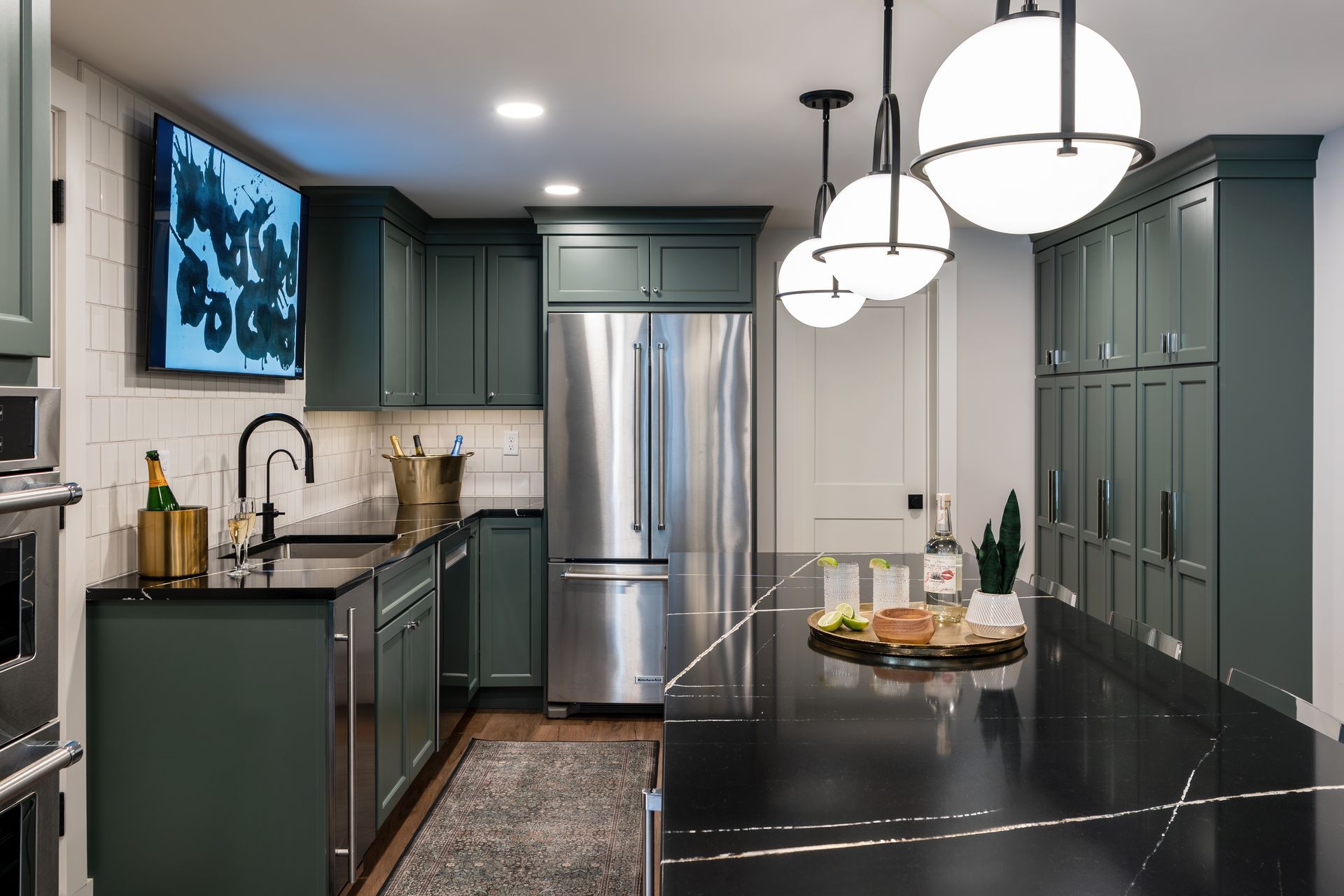 Modern kitchen with dark green cabinets, stainless steel fridge, black island, and pendant lights