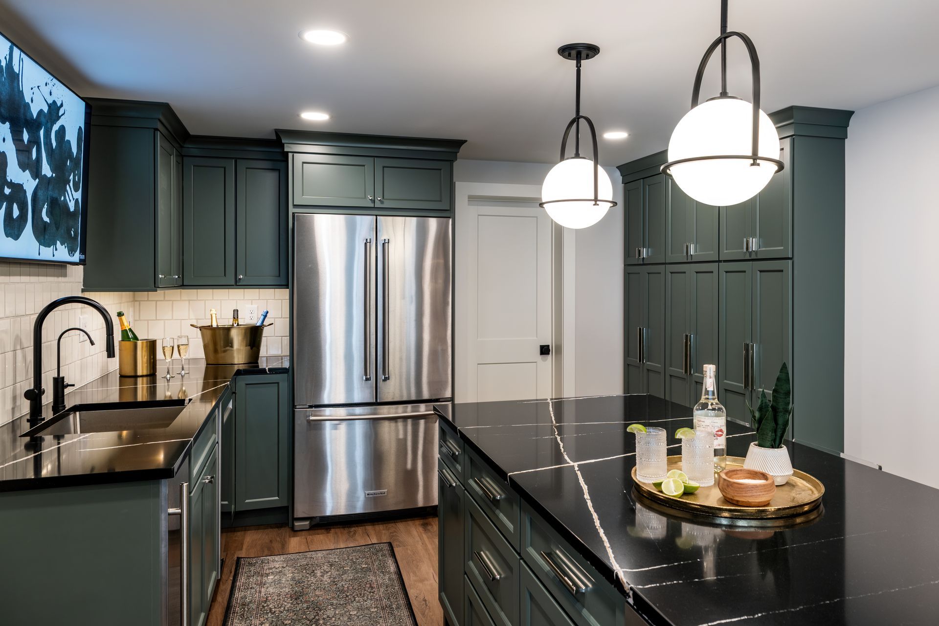 Modern dark-green kitchen with stainless steel appliances, black countertops, and pendant lights