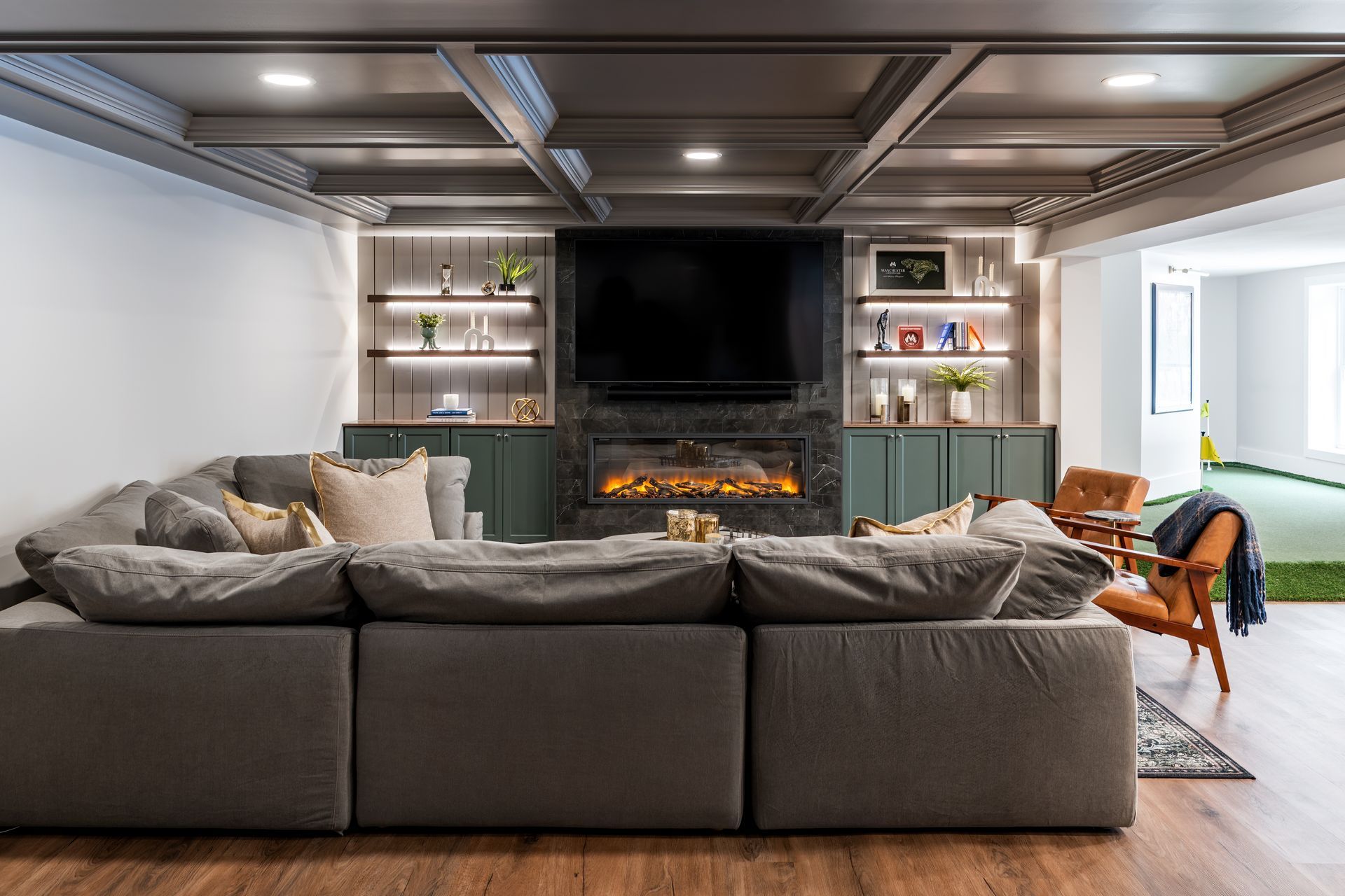 Modern living room with a large gray sectional, fireplace, TV, built-in shelves, and wood flooring