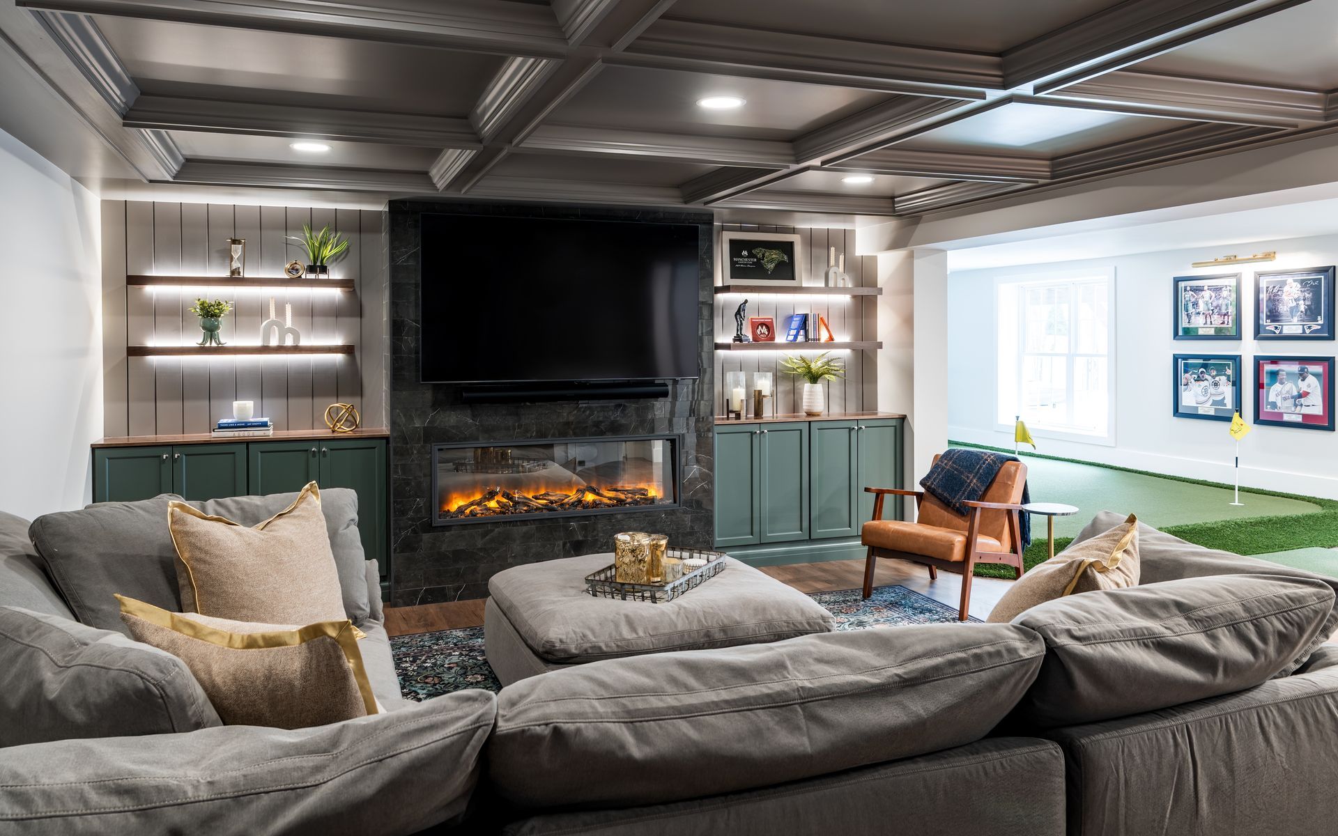 Modern living room with gray sectional, fireplace, large TV, and bright windows over a green rug