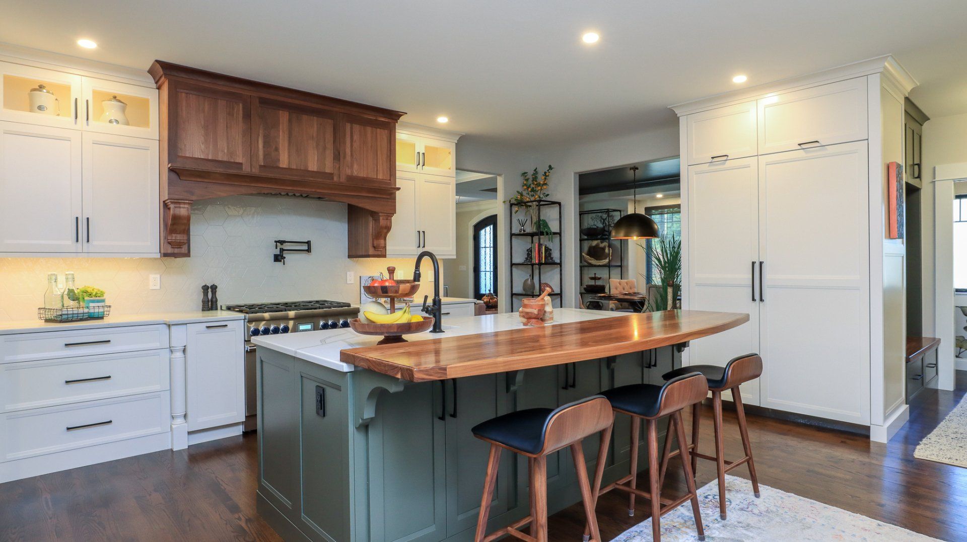 Bright modern kitchen with white cabinets, large island, wooden stools, and dark hardwood floors.