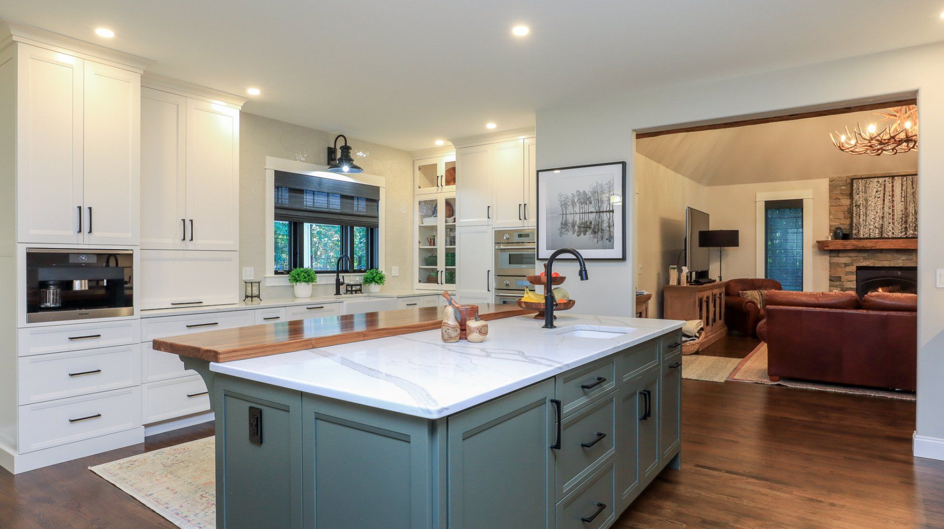 Bright white kitchen with blue island opening to a living room and hardwood floors
