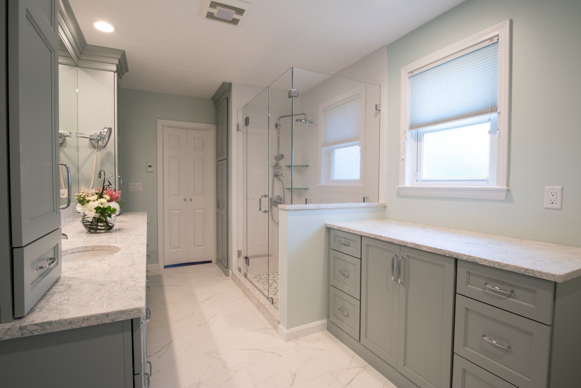 Bright modern bathroom with gray cabinets, double vanity, shower, and two windows