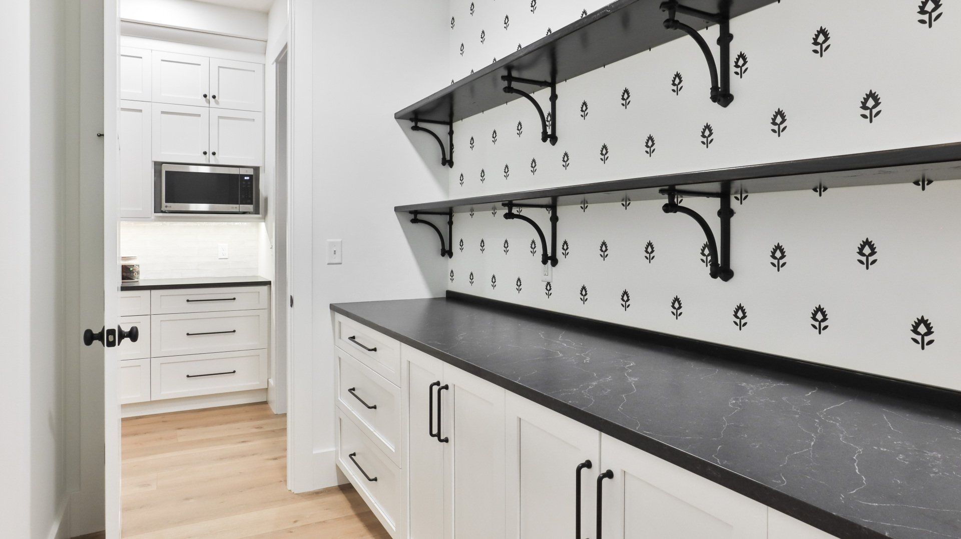 Bright white laundry room with black shelving, countertops, cabinets, and a doorway to a kitchen