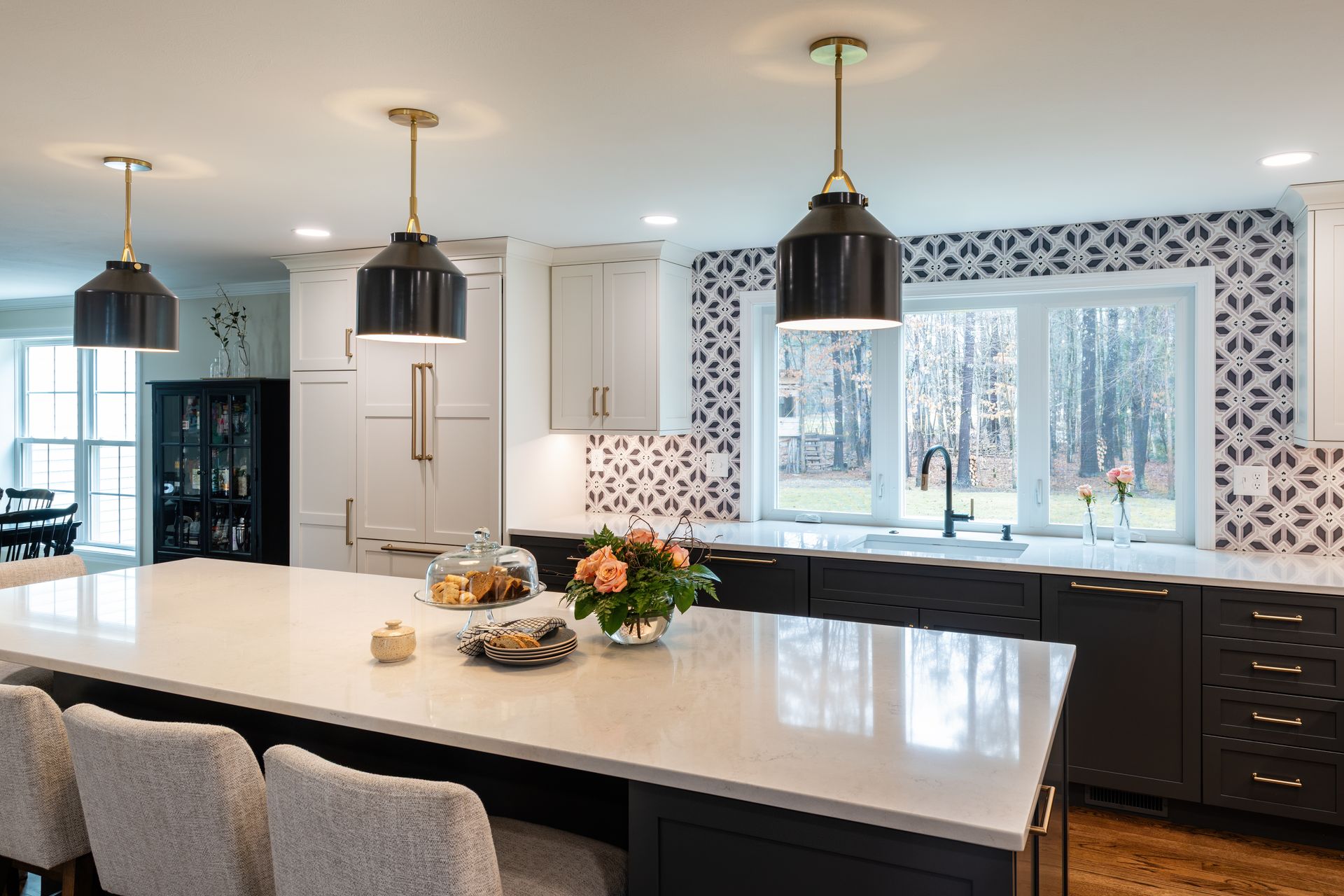 Modern kitchen with large island, pendant lights, dark cabinets, and windows overlooking trees
