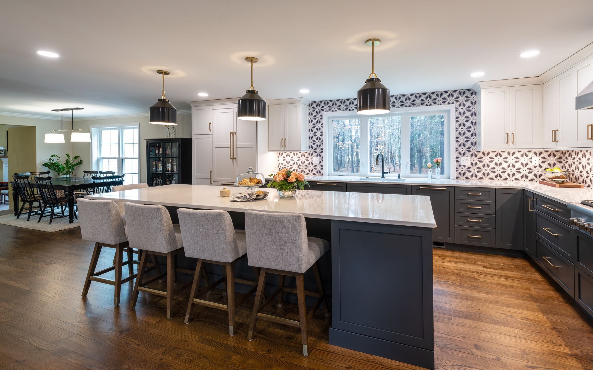 Modern kitchen with large island, pendant lights, dark cabinets, and patterned backsplash by a dining area