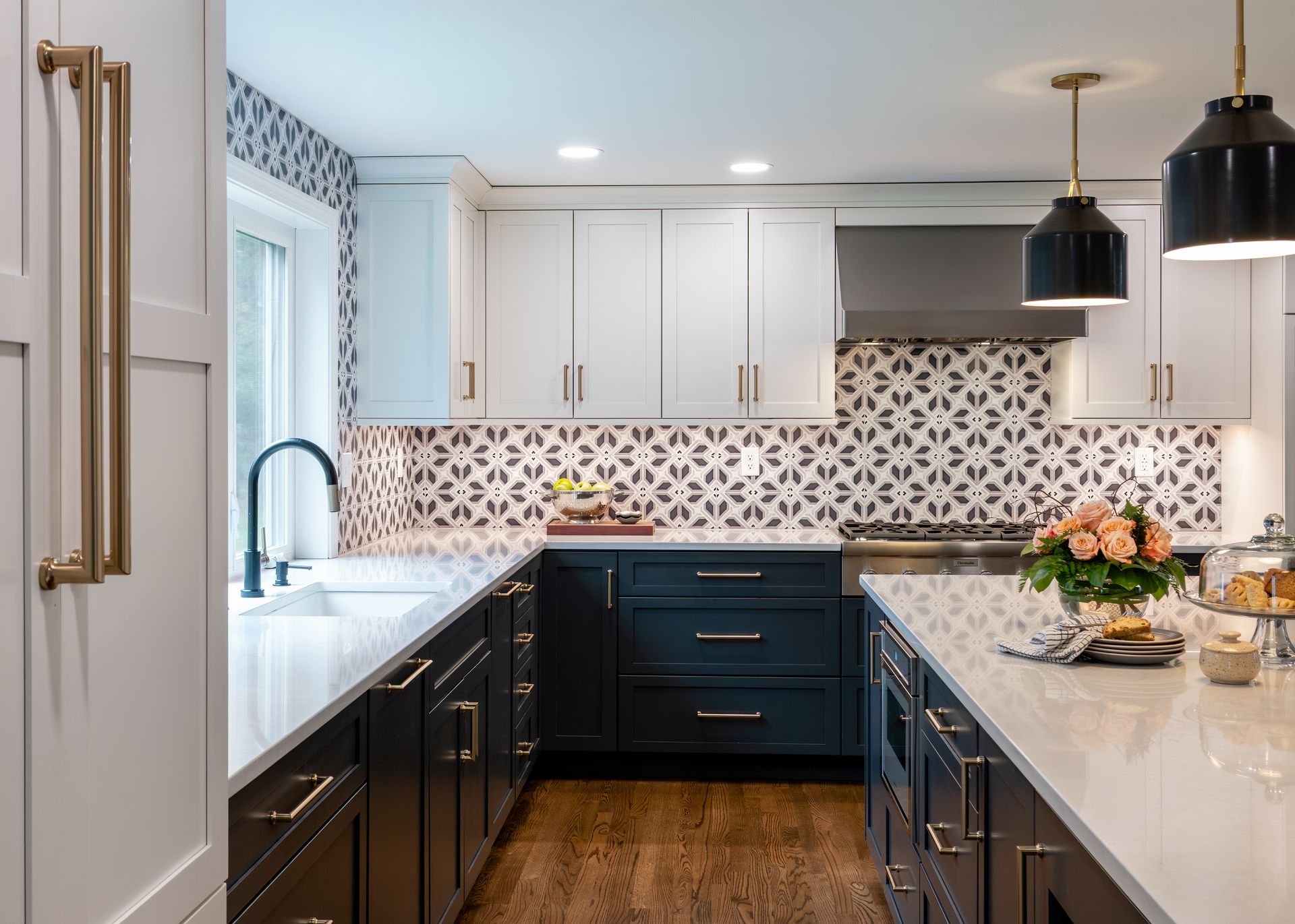Modern kitchen with white cabinets, dark island, patterned backsplash, brass fixtures, and flowers on the counter