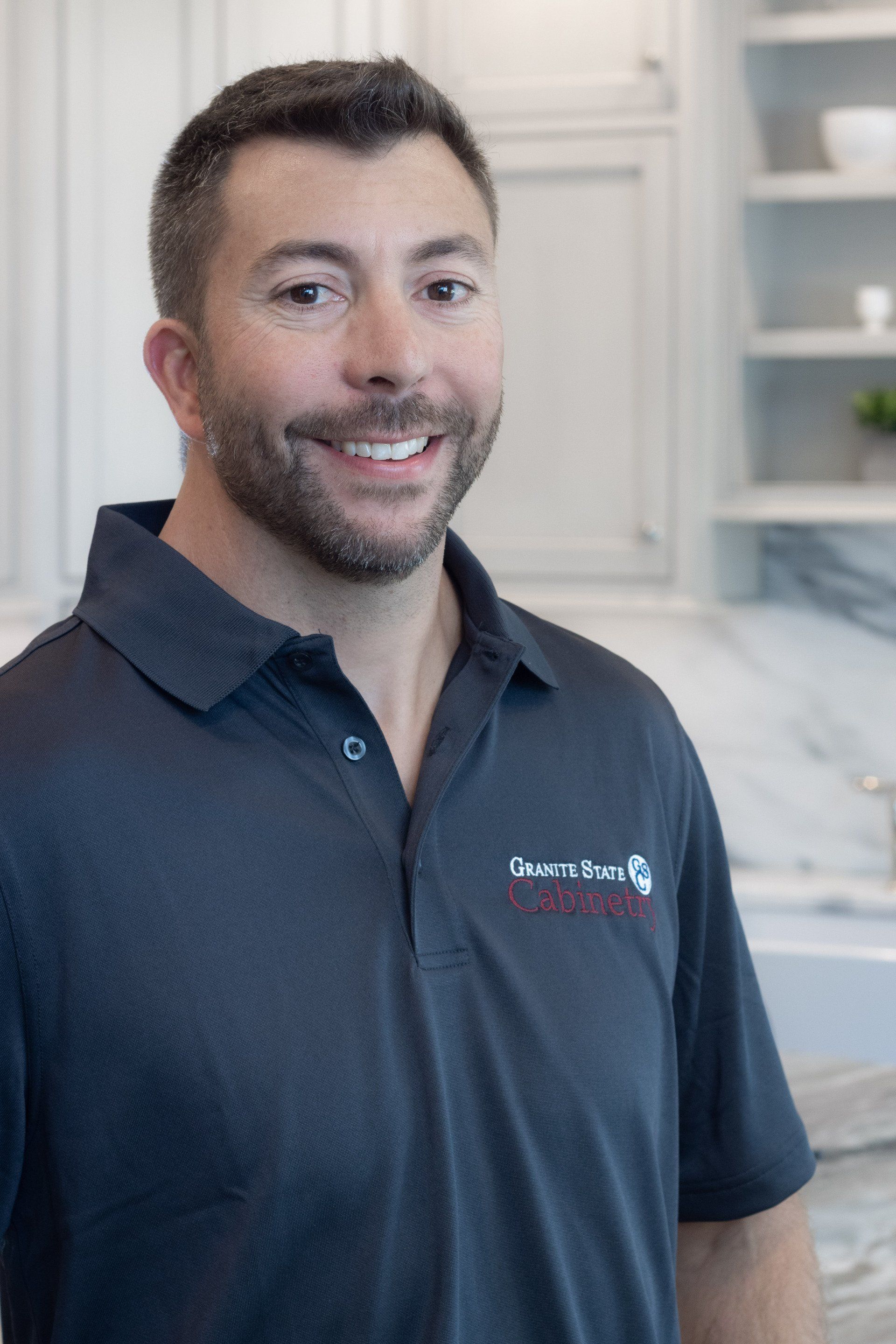 Smiling man in a dark polo shirt standing in a bright kitchen-like interior.
