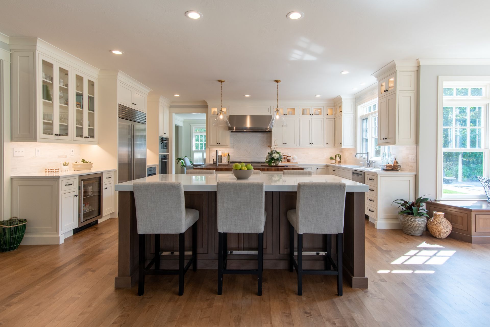 Modern white kitchen with island, gray stools, hardwood floors, and bright natural light