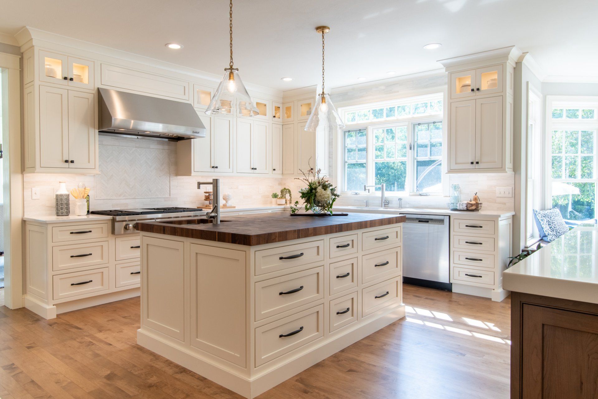 Bright white kitchen with a large island, wood countertop, pendant lights, and sunlit windows.