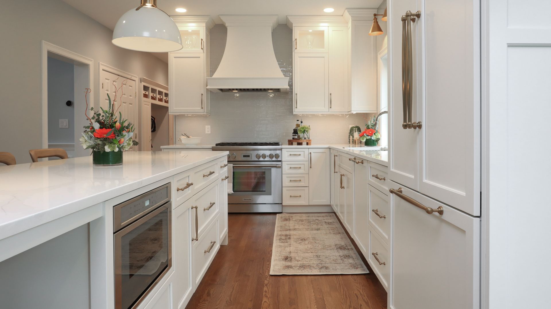 Bright white kitchen with island, stainless appliances, wood floor, and a small rug and flowers