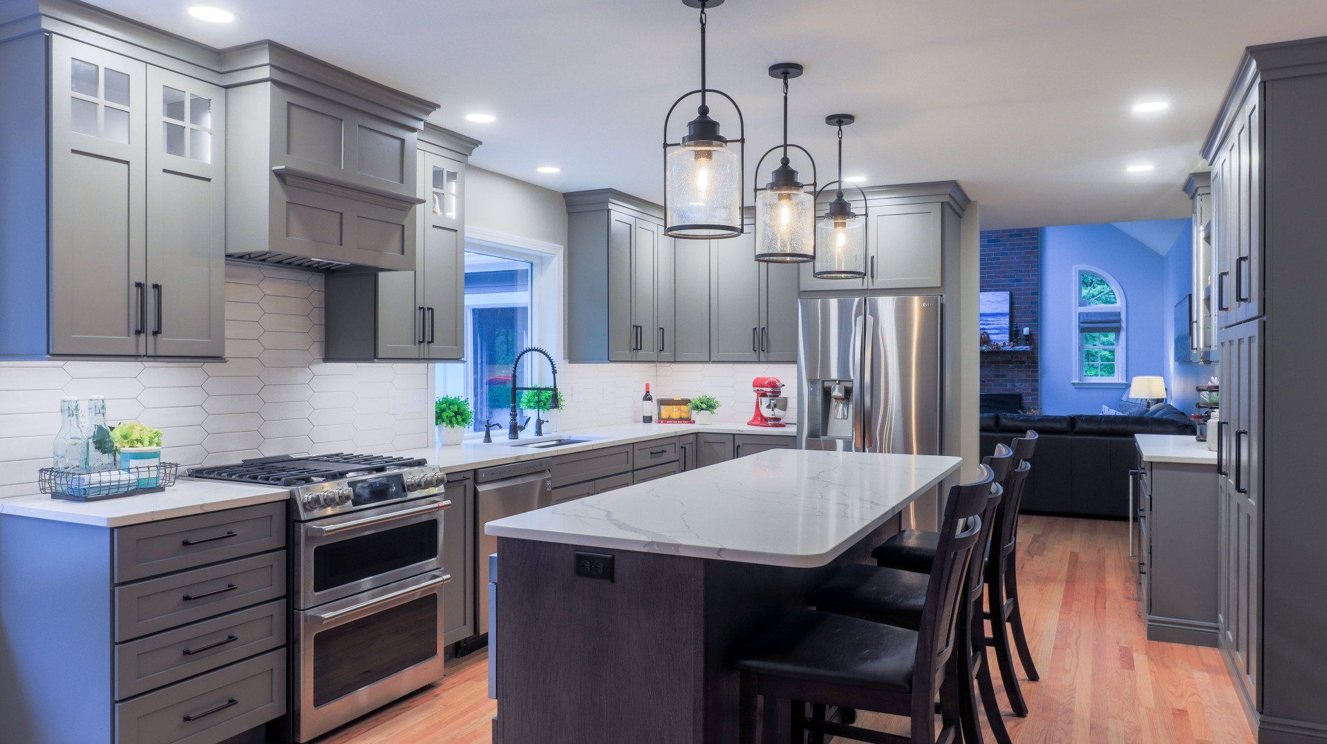 Modern kitchen with gray cabinets, white island, pendant lights, and stainless steel appliances