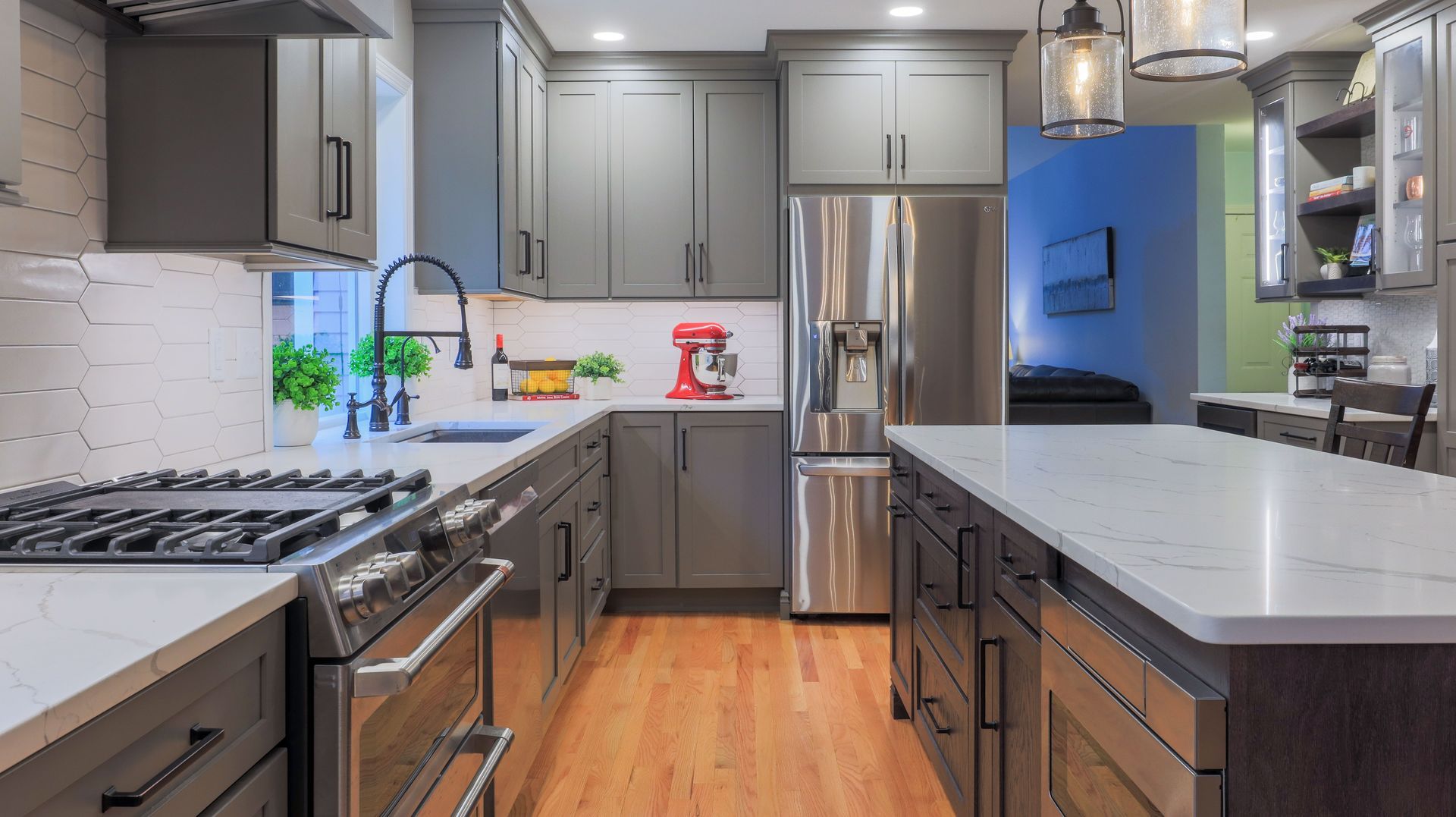 Modern kitchen with gray cabinets, stainless steel appliances, wood floors, and a white tile backsplash