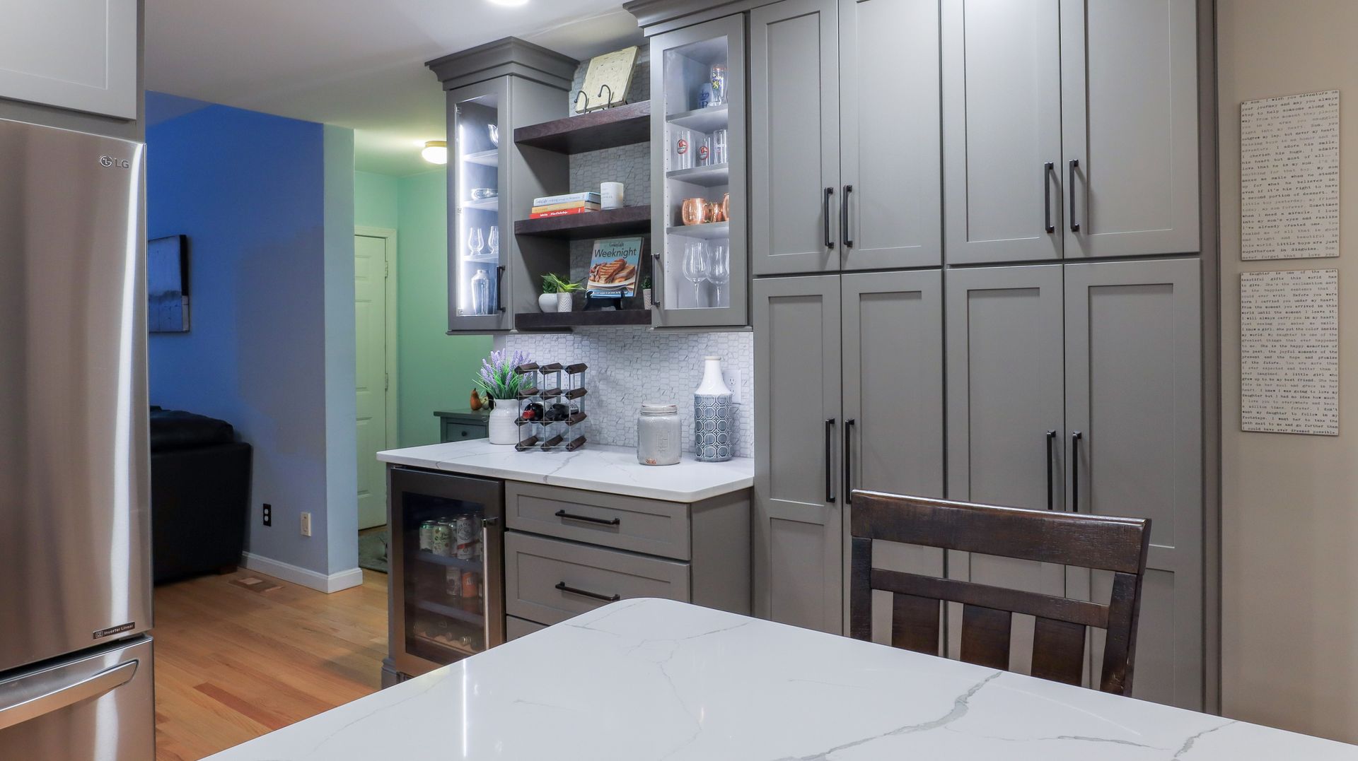 Modern kitchen with gray cabinets, white island counter, and a partially open pantry display.