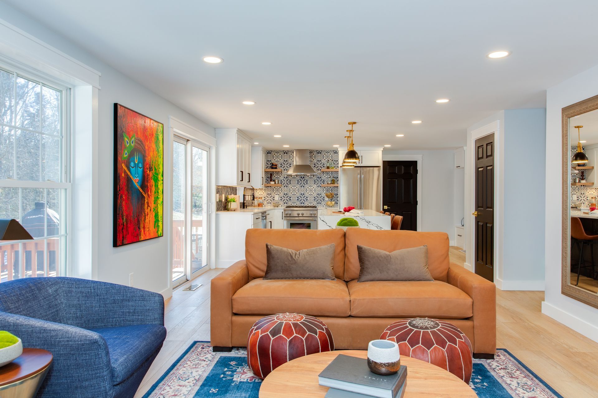 Bright modern living room with orange sofa, blue chair, colorful art, and open kitchen in the background