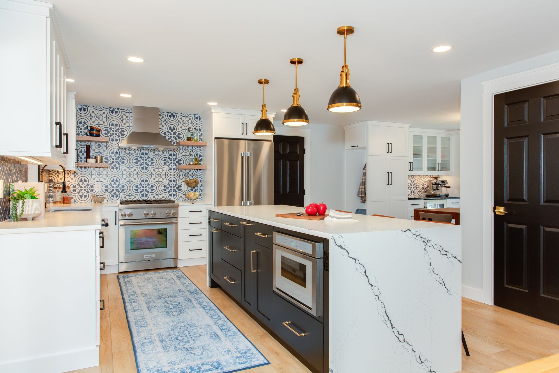 Bright modern kitchen with marble island, dark cabinets, brass pendants, and patterned tile backsplash