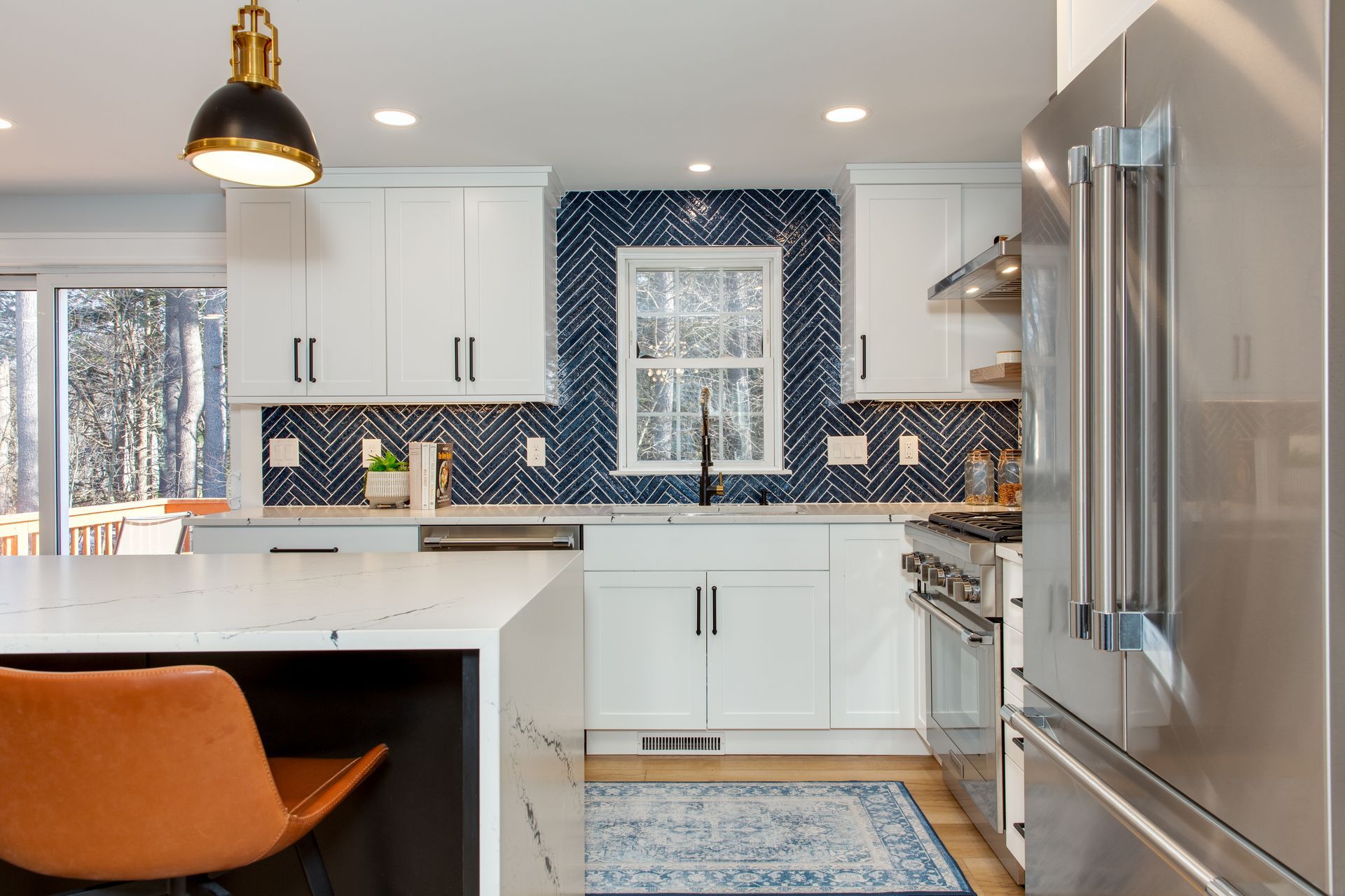 Modern kitchen with white cabinets, navy patterned backsplash, stainless steel fridge, and orange island chair